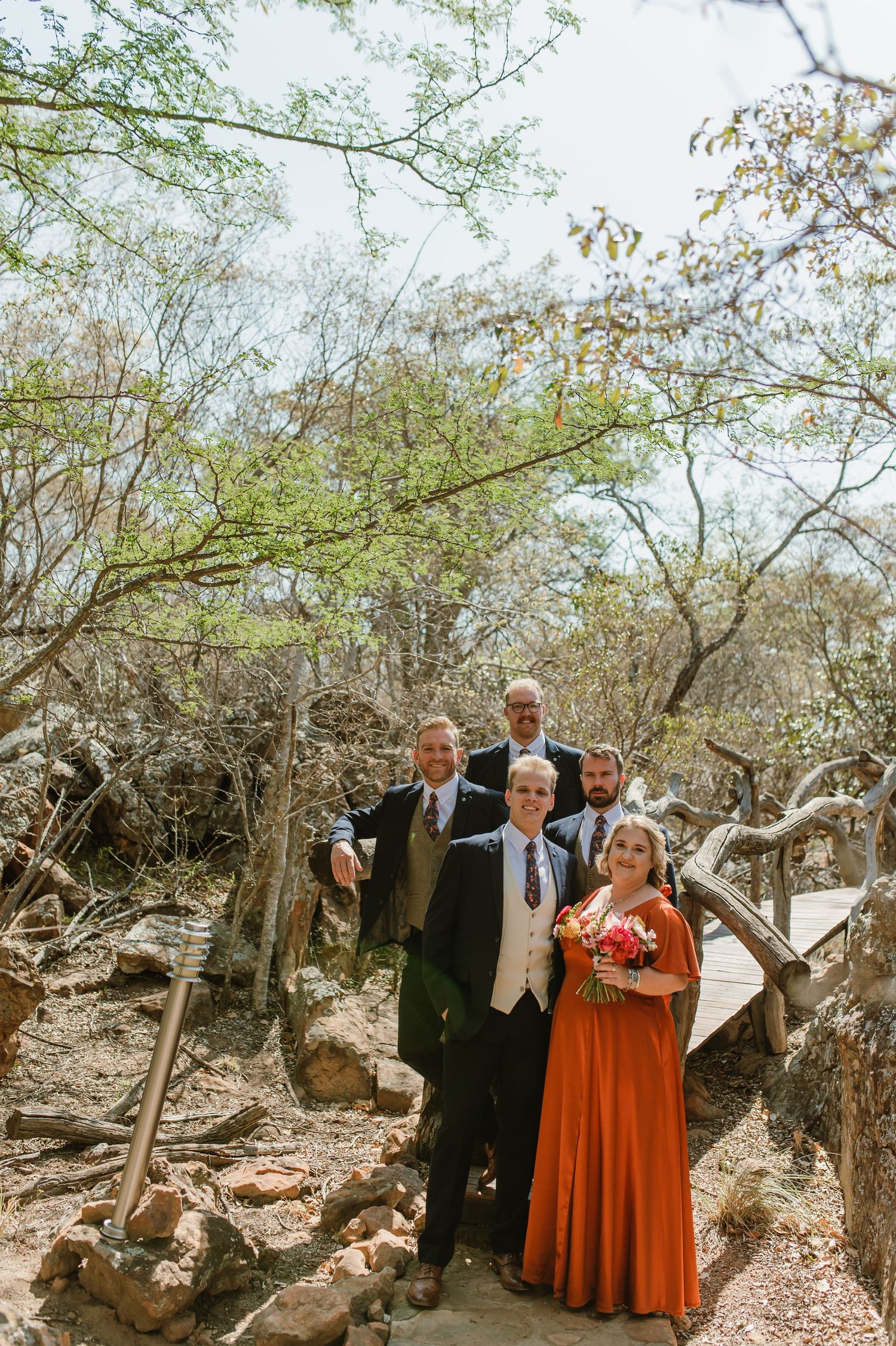A small wedding group poses on rocky outdoor steps surrounded by winter trees.