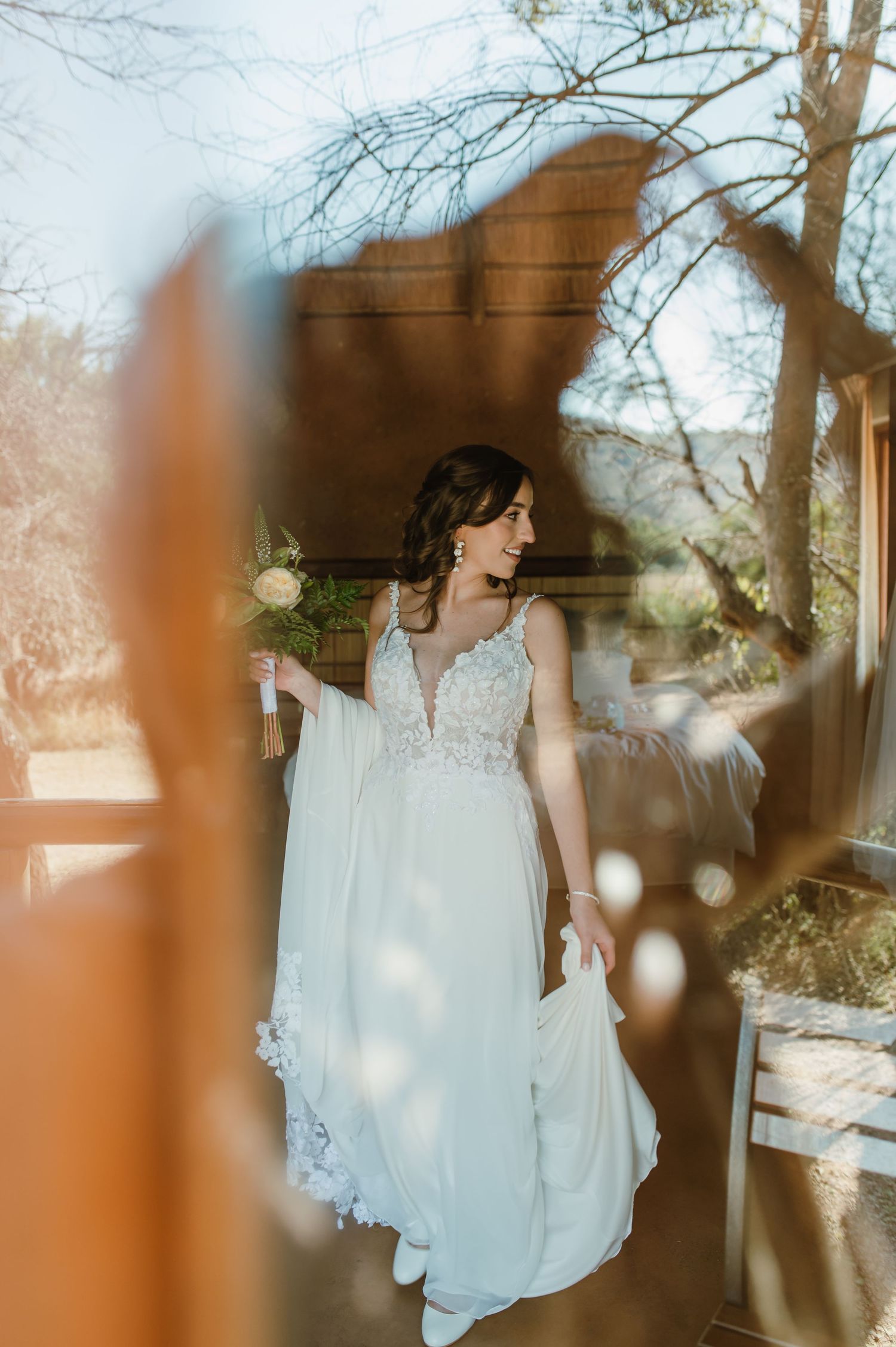 Sunlit wedding dress photographed through window reflections creating artistic effect.