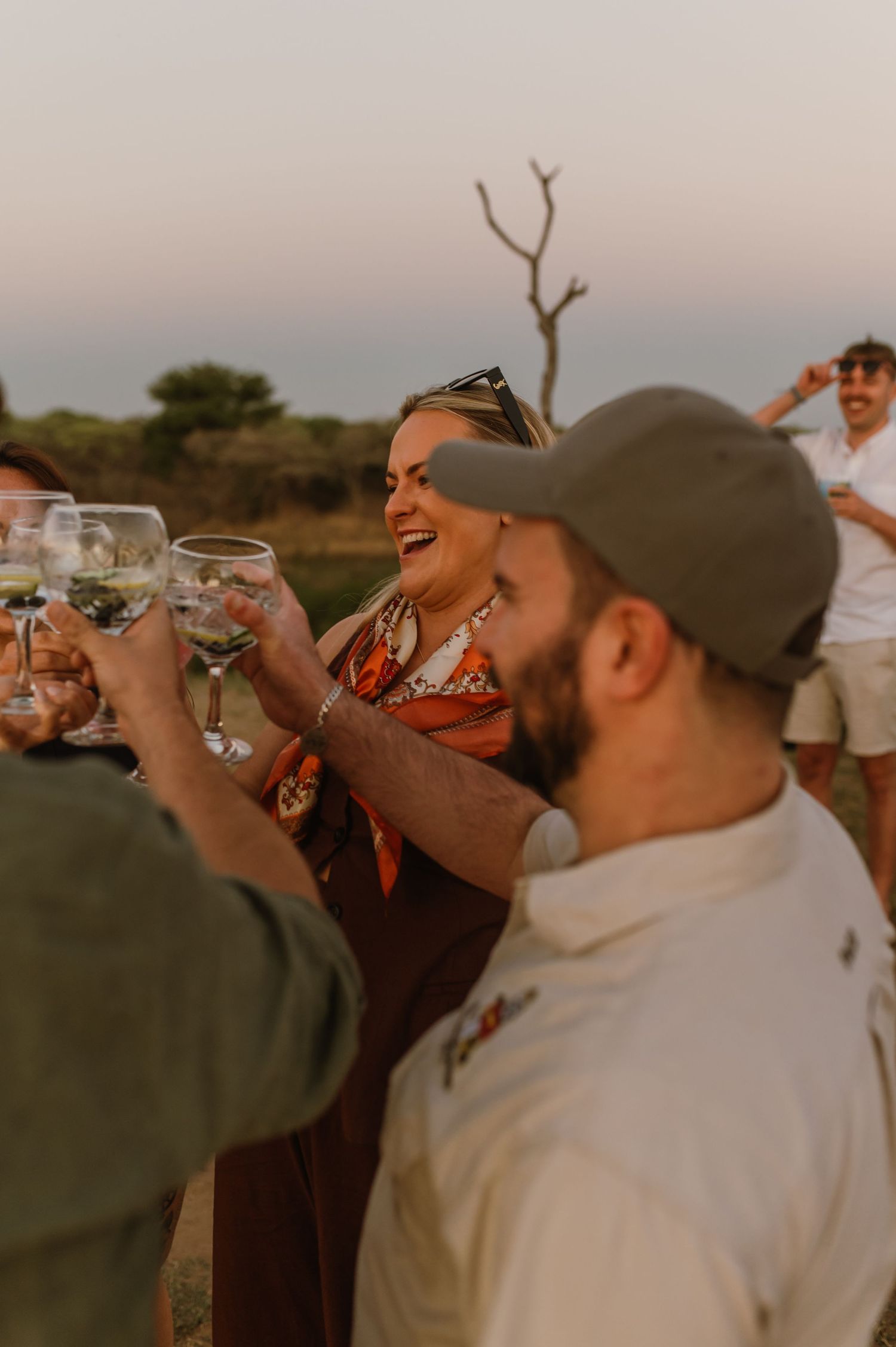 Friends raising wine glasses together in a celebratory toast at sunset.