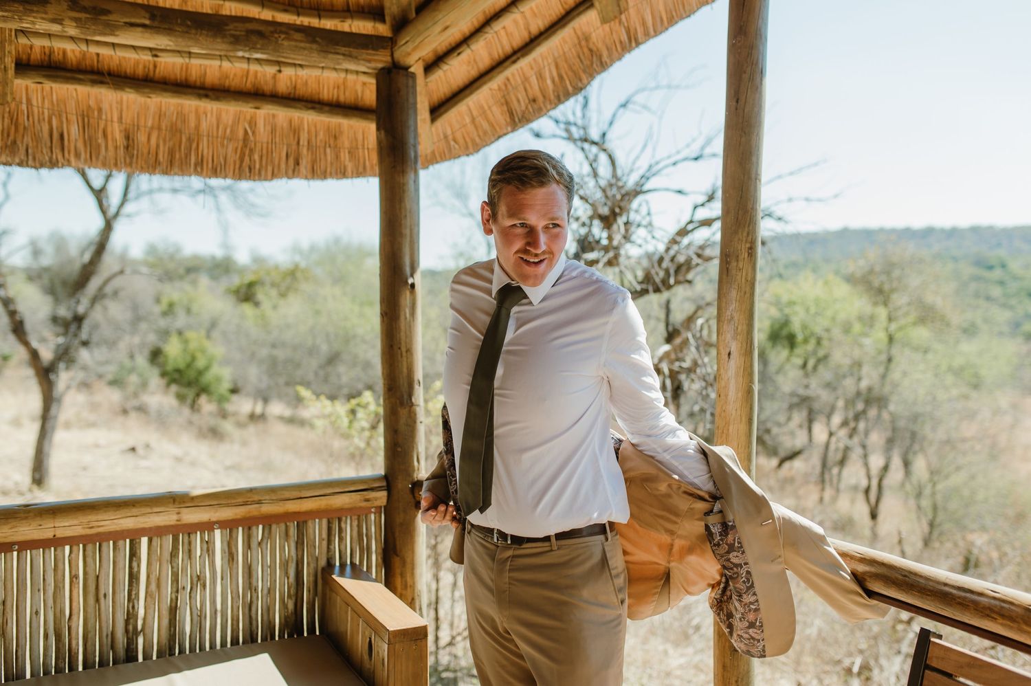 Wedding party members relax on a thatched-roof veranda with scenic savanna views.