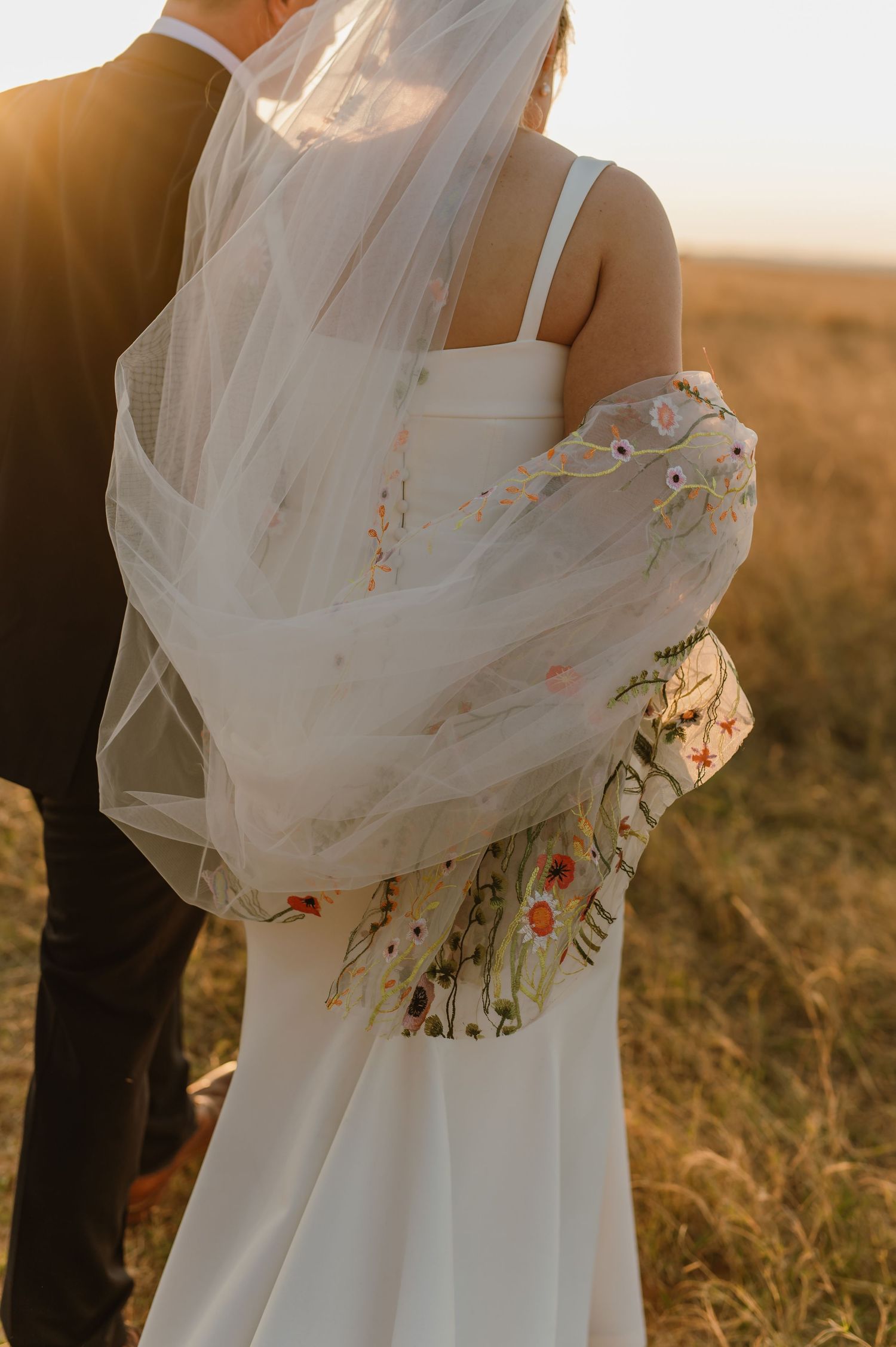 Close-up details of a flowing wedding veil with floral embellishments in sunset light.