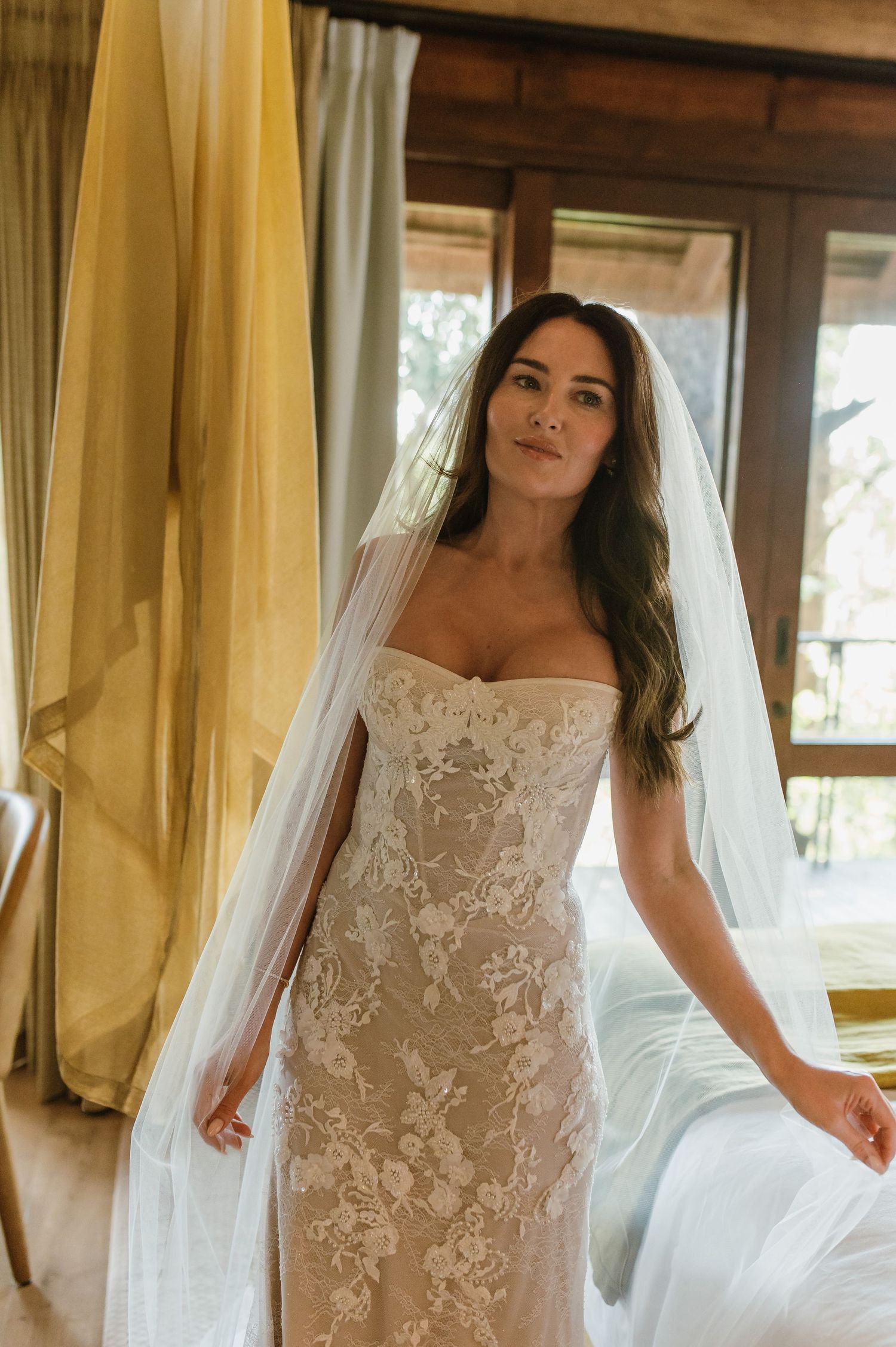 Stunning bride wearing a strapless lace wedding gown and flowing veil in a warm safari lodge suite.