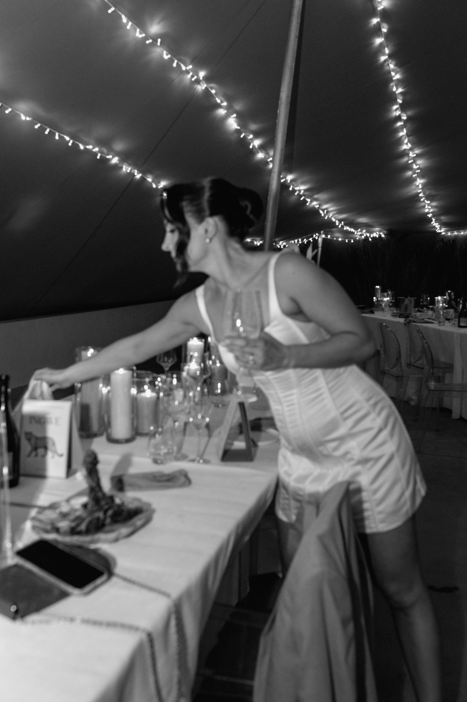 Black and white photo of wedding guests dancing at reception under string lights.