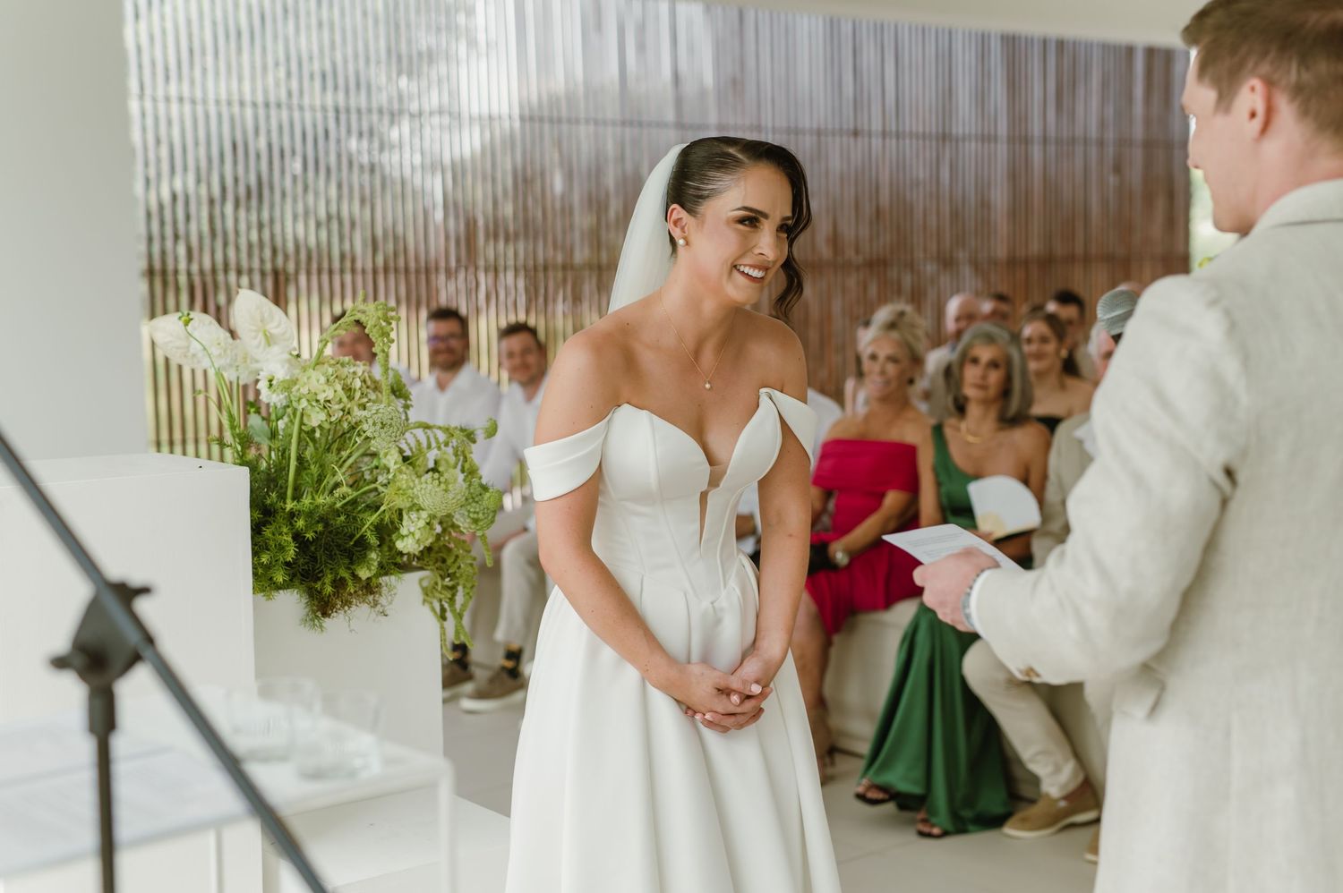 A wedding ceremony in progress with guests watching in a modern white interior space.