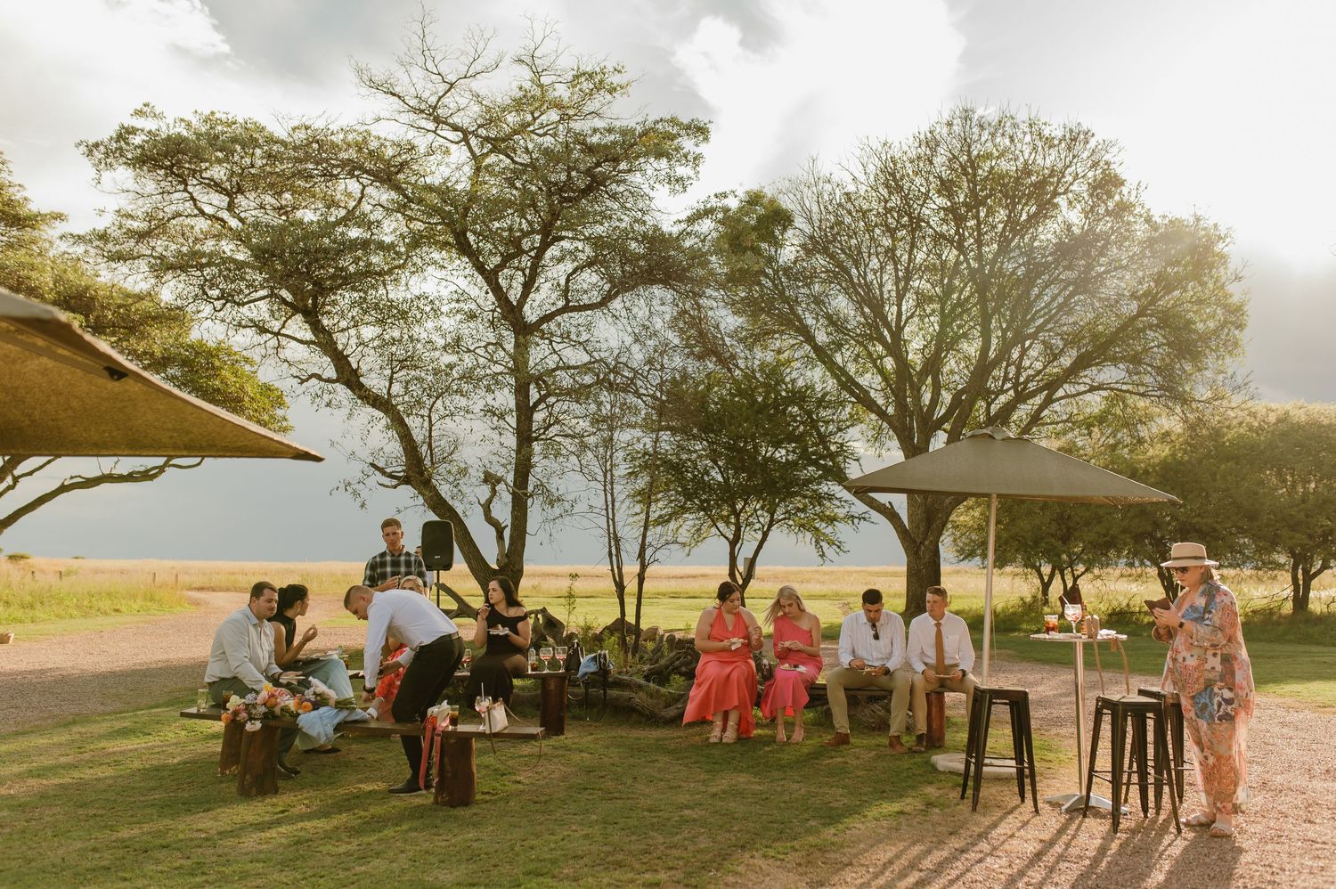 Wedding guests mingling under shade trees at elegant outdoor bush wedding reception venue.