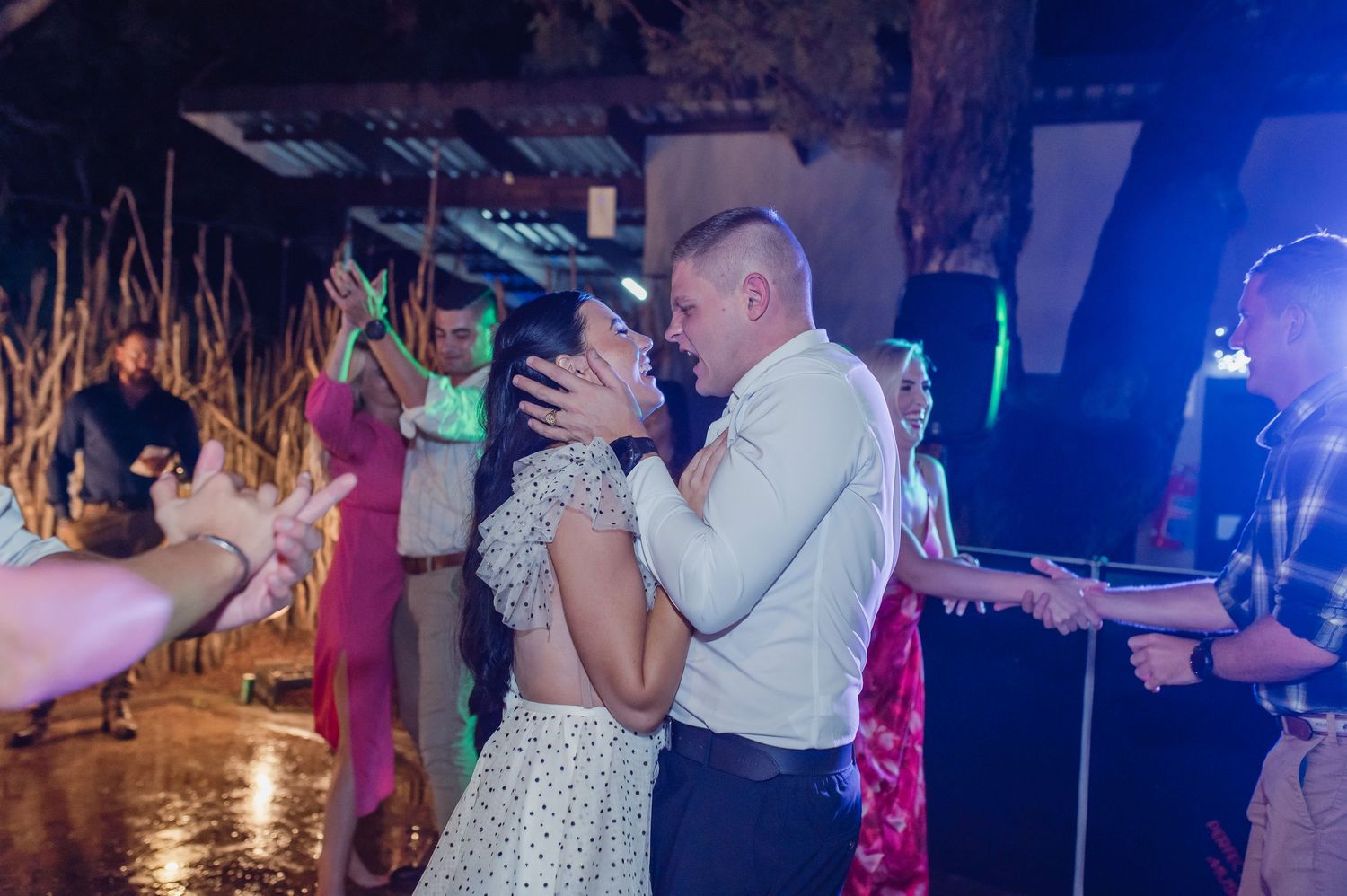 Bride and groom sharing a kiss on the dance floor surrounded by celebrating wedding guests.