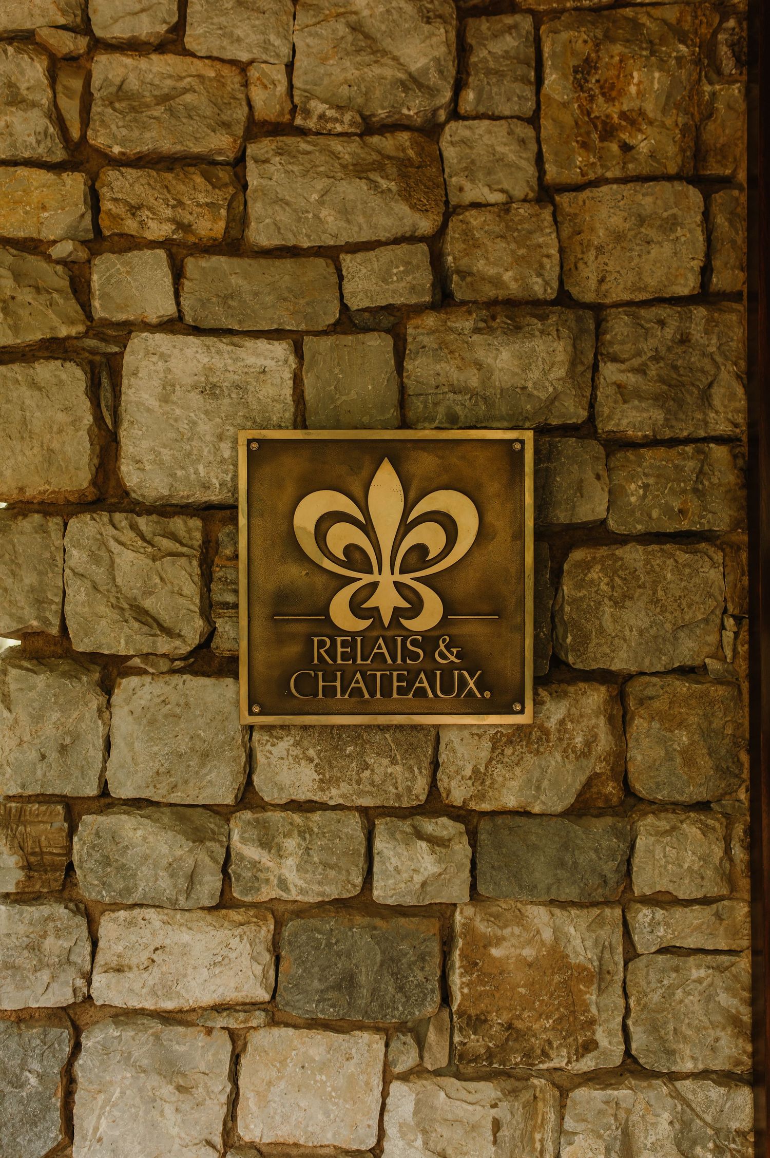 Gold Relais & Chateaux plaque mounted on a rustic stone wall at a luxury lodge.