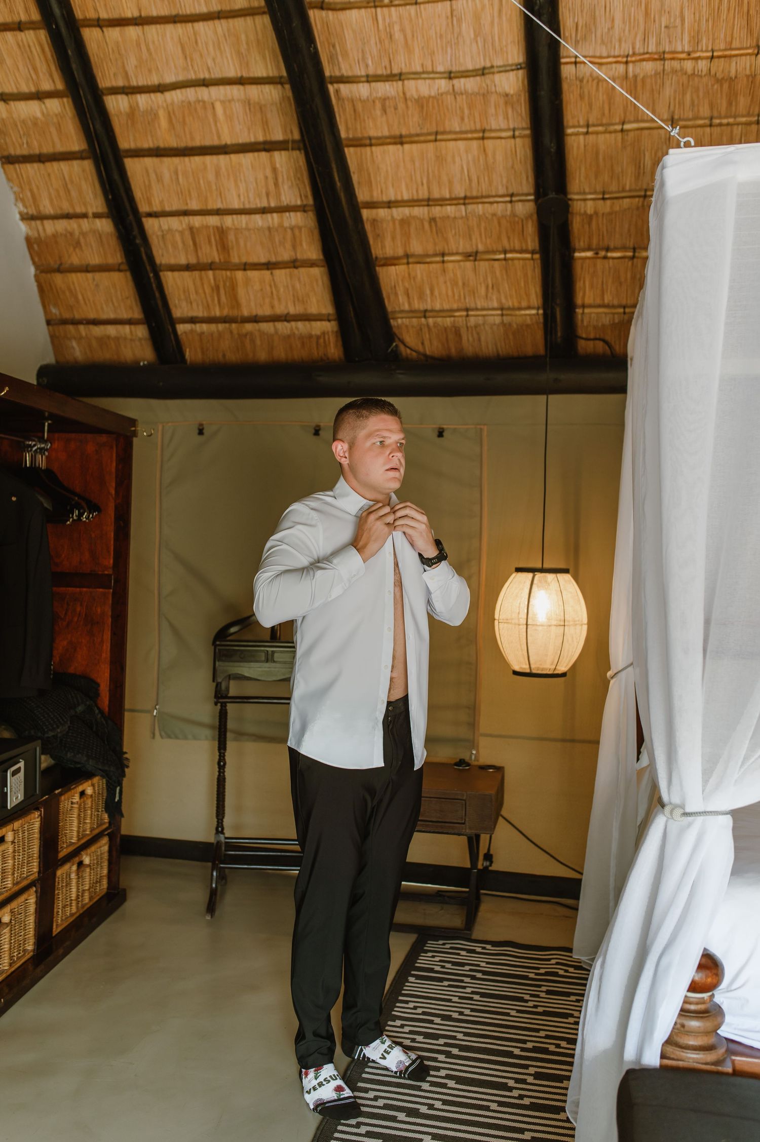 Groom adjusting his tie while getting dressed in a rustic safari lodge room before his wedding.