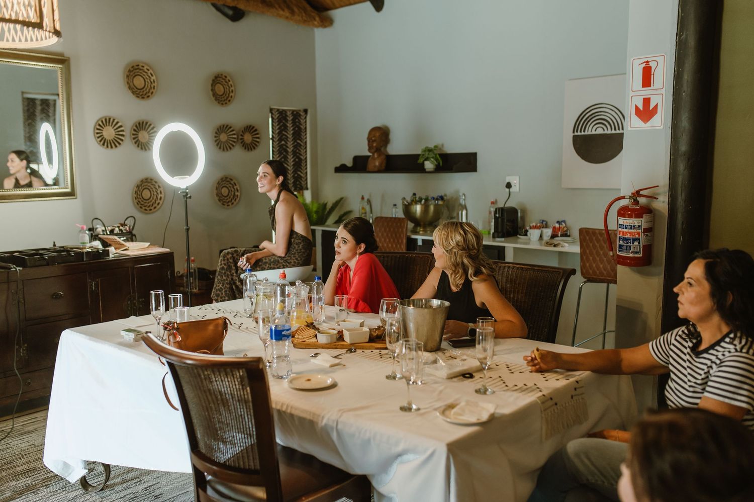 Women gathered around a dining table with glassware in a rustic room with ring light and decor.