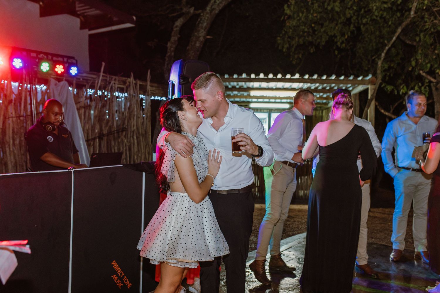 Bride and groom sharing a dance at lively outdoor wedding reception with DJ and colorful disco lights.