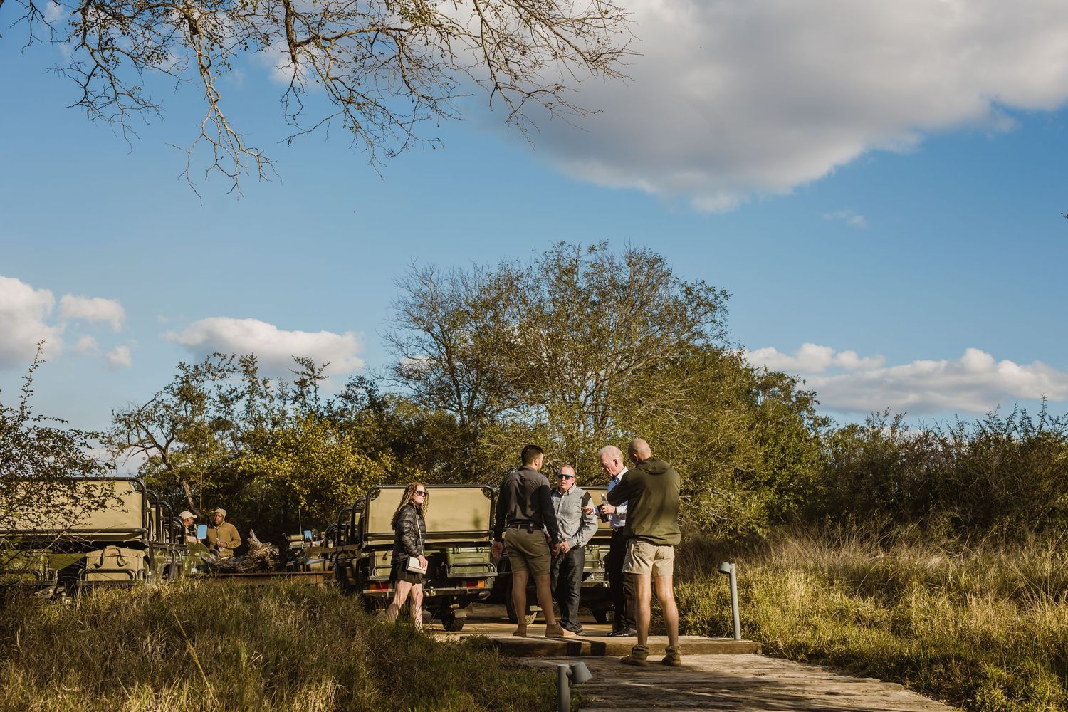 Safari tourists observe wildlife from elevated viewing vehicles in a natural game reserve setting.