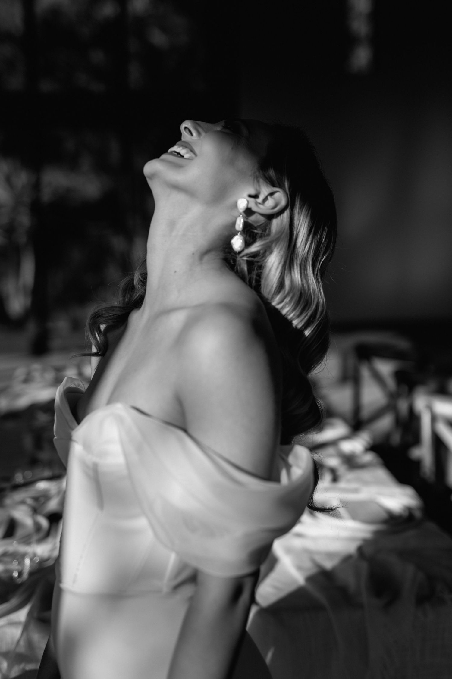 Artistic black and white portrait of a woman in an off-shoulder dress with her head tilted back.