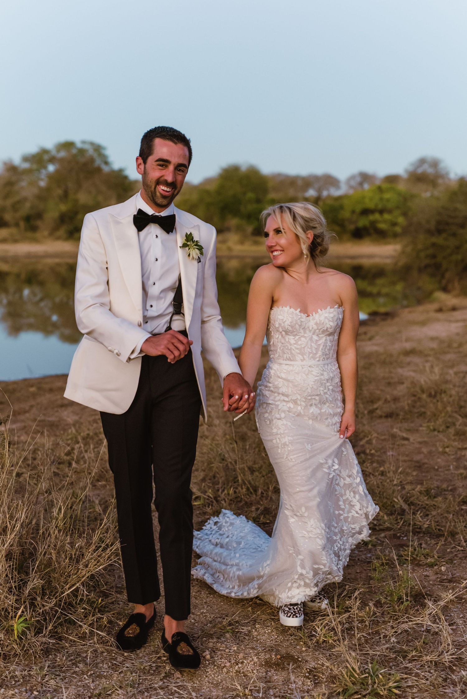Playful newlyweds walk hand in hand along a coastal path.