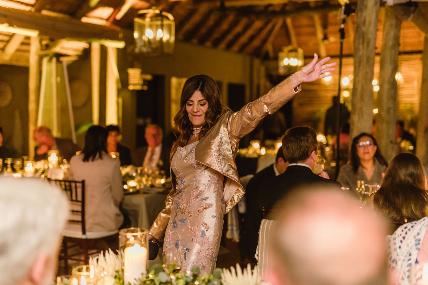 Guest dancing with raised arms during reception in rustic venue with ambient lighting.