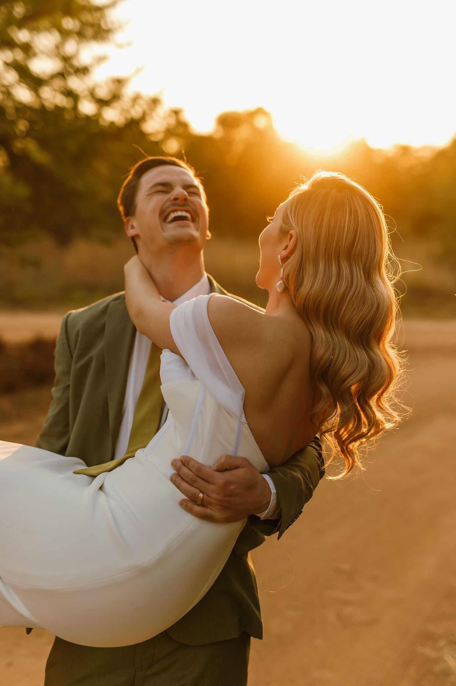 Playful couple laughing and embracing during sunset photoshoot outdoors.