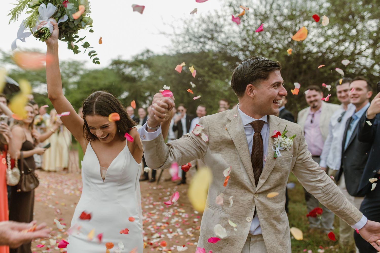 Guests toss coral-colored flower petals during outdoor wedding celebration.