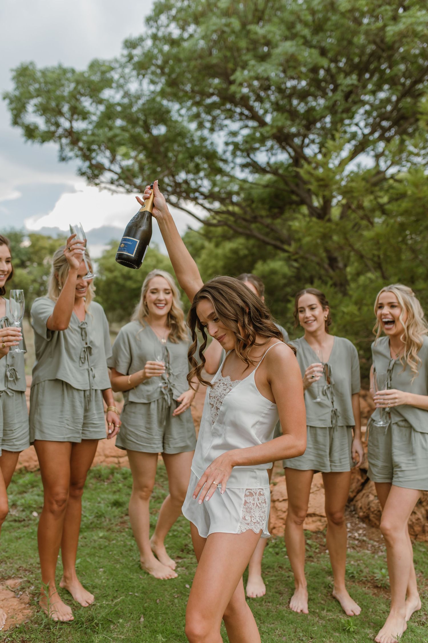 Group celebration with drinks on a grassy hillside during a wedding event.