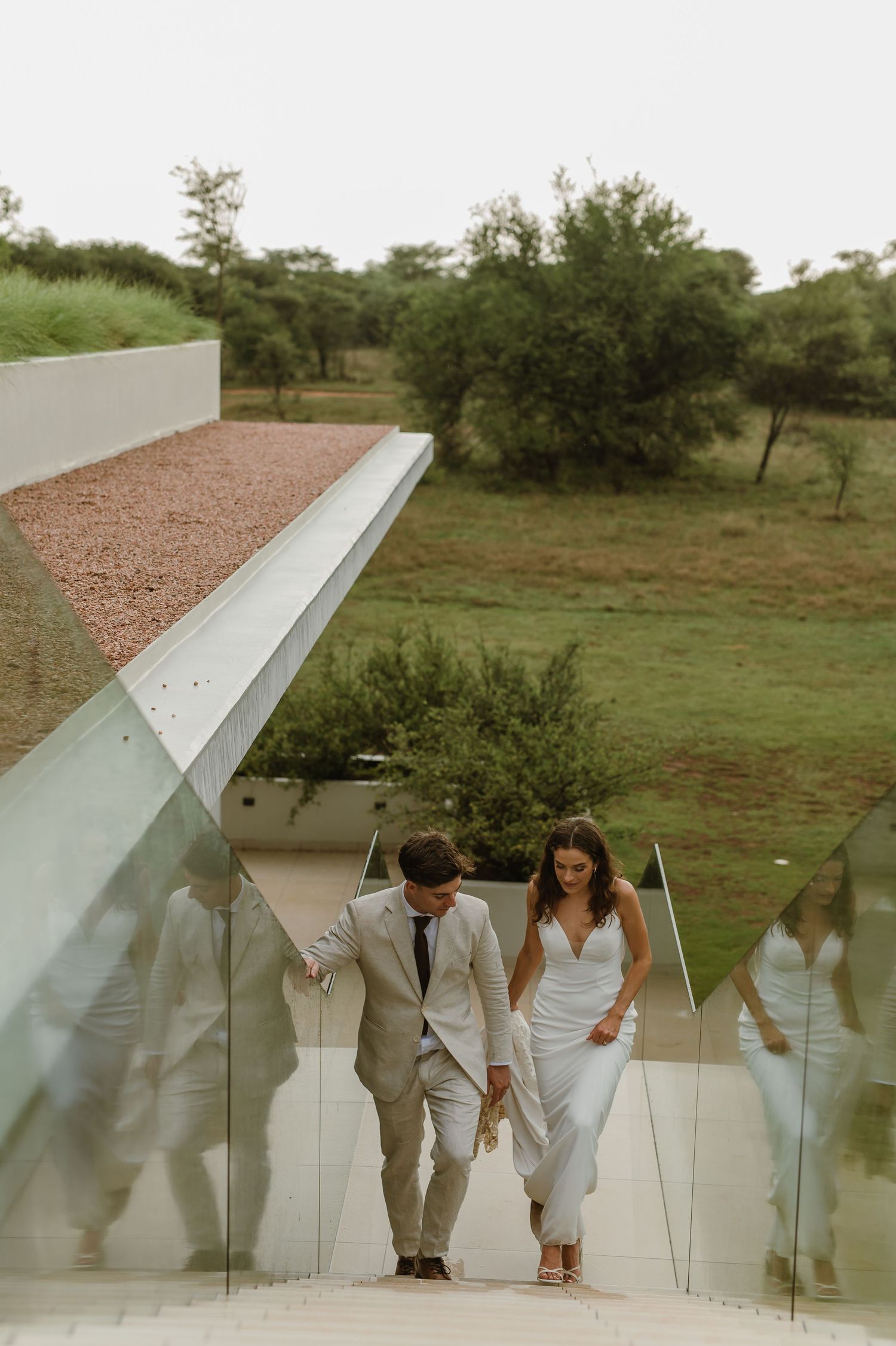 Stylish wedding couple walking along a modern concrete structure with natural surroundings.
