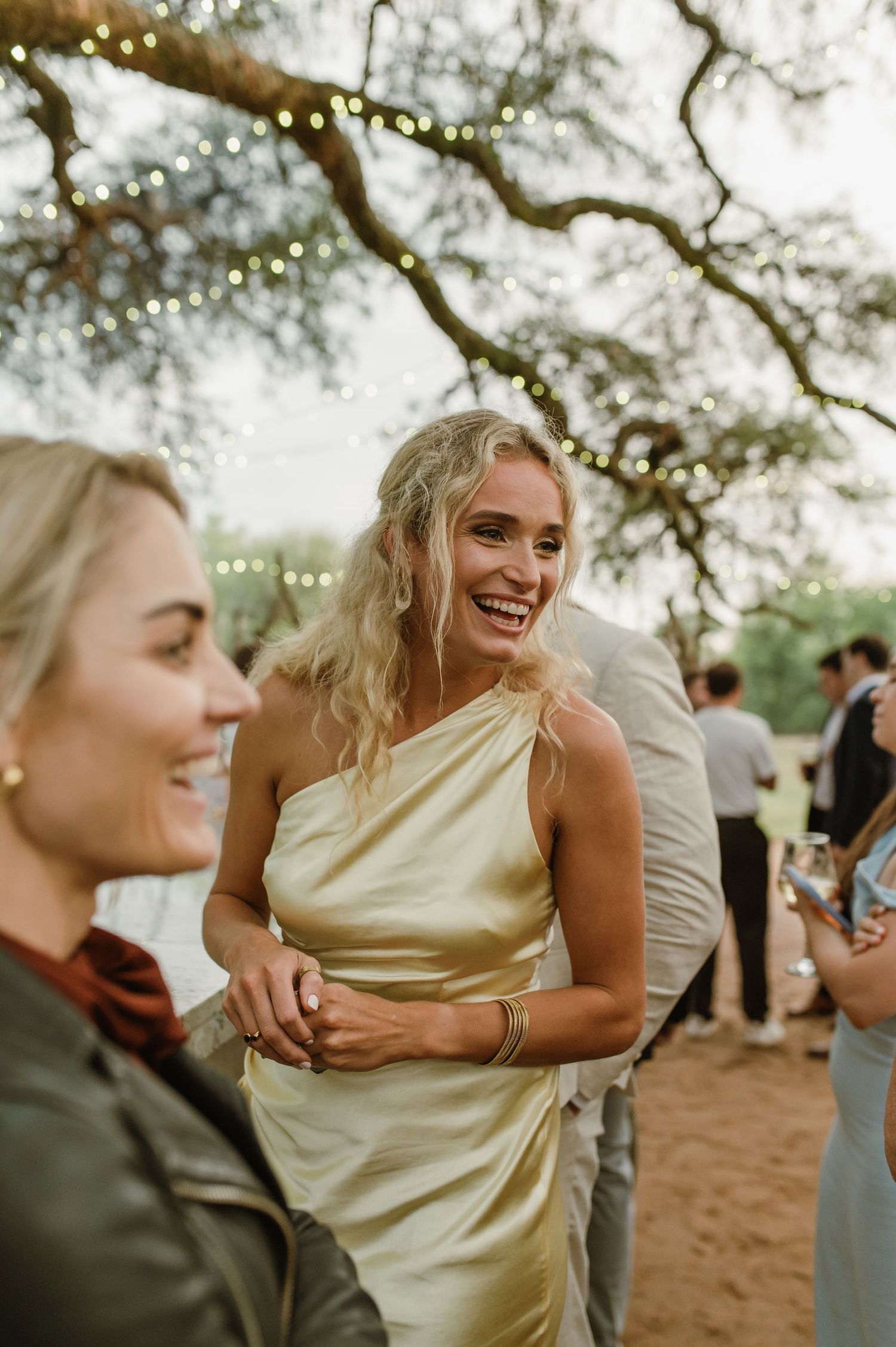 Wedding party members in light colored dresses sharing joyful moments outdoors.