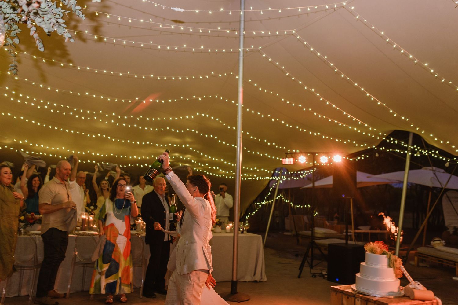 Romantic string lights create a magical ambiance at an outdoor evening wedding reception.