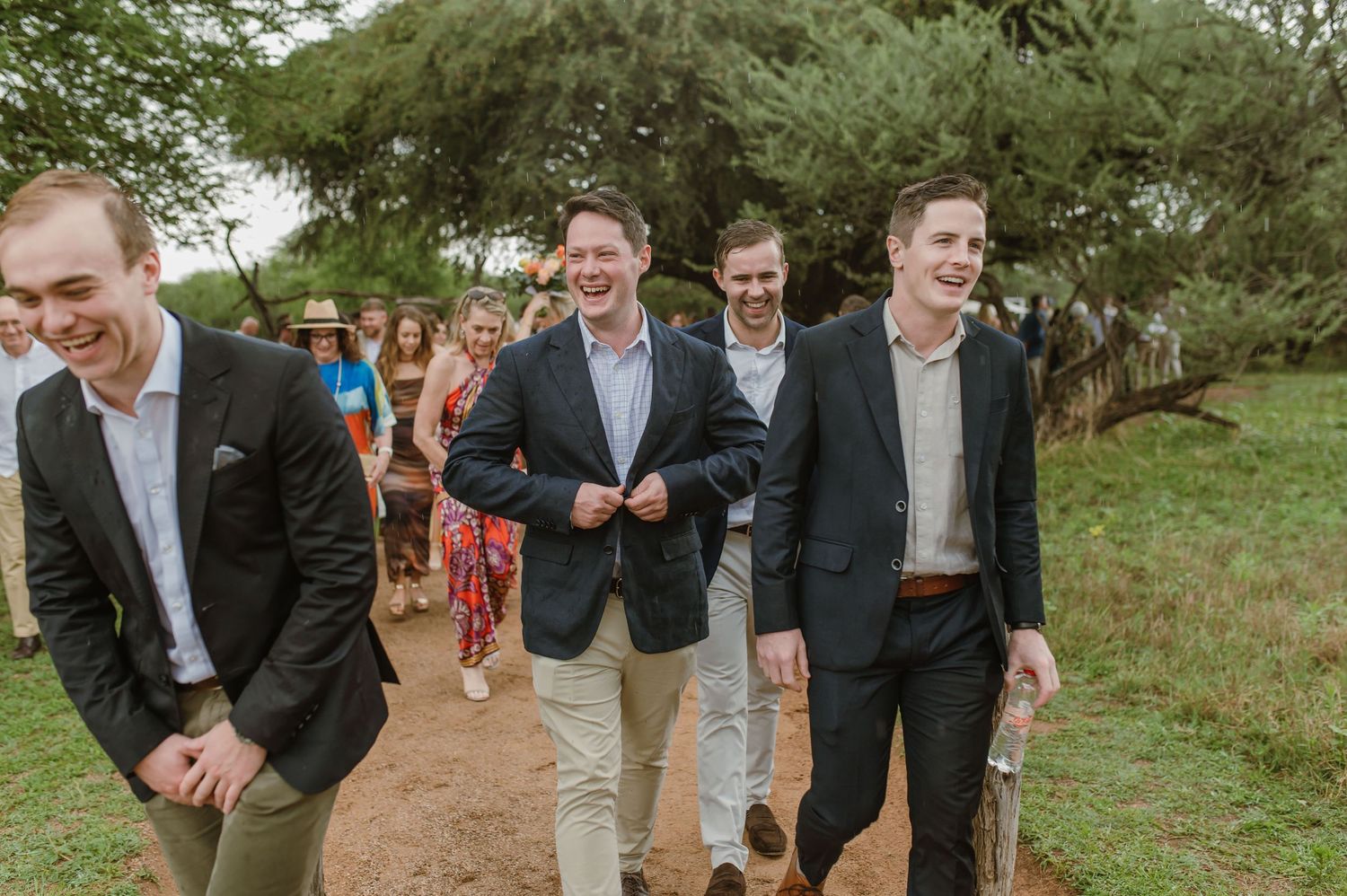 Wedding guests in dark suits walking along a rustic outdoor path.