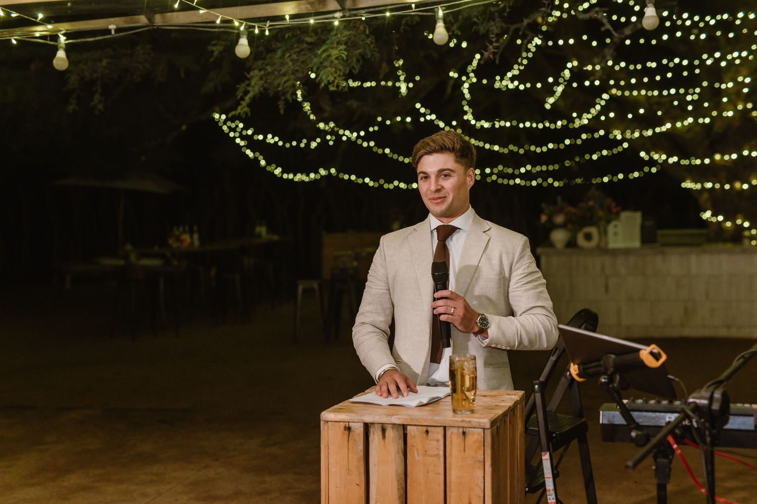 Wedding reception venue decorated with twinkling string lights and wooden podium for speeches.