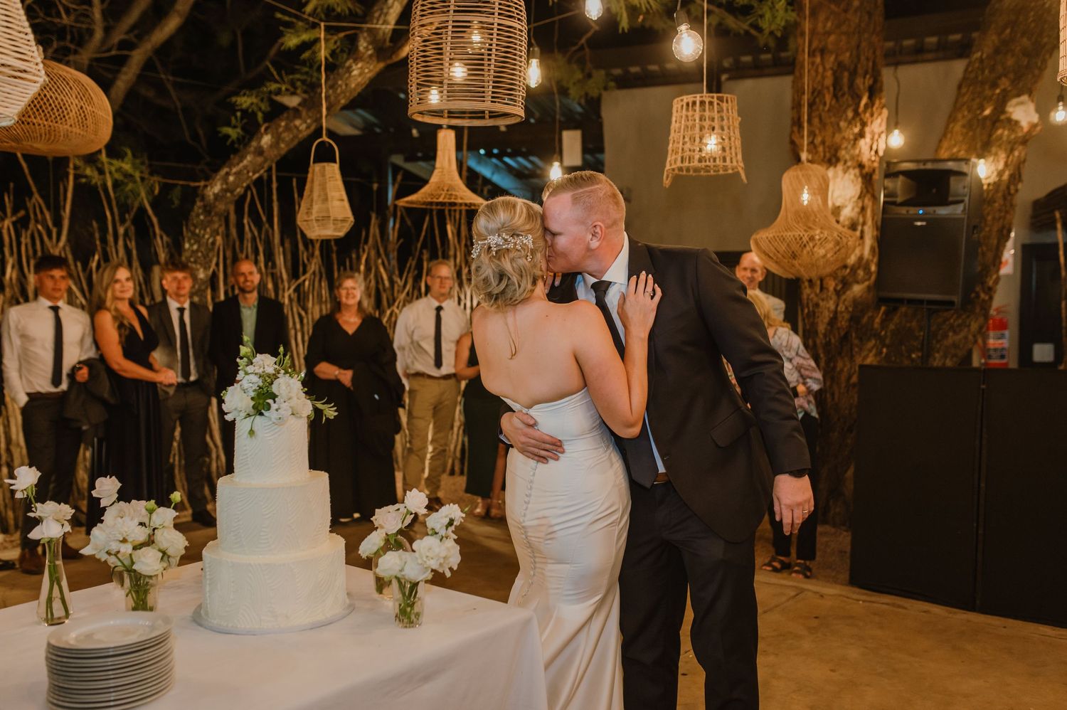 Evening wedding reception with string lights and rattan pendants creating a romantic atmosphere.