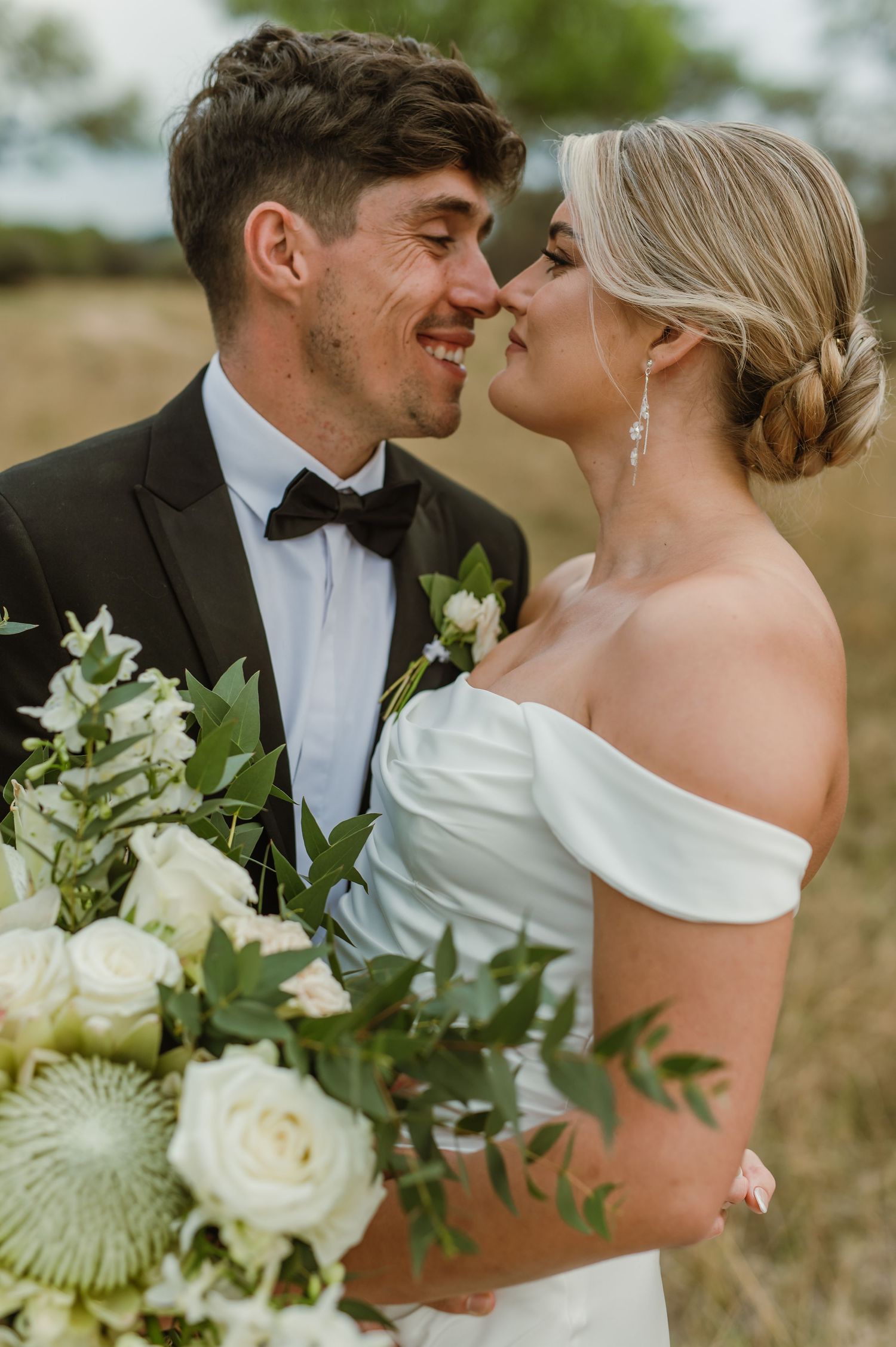Close-up of newlyweds sharing tender moment with white roses and greenery bouquet.