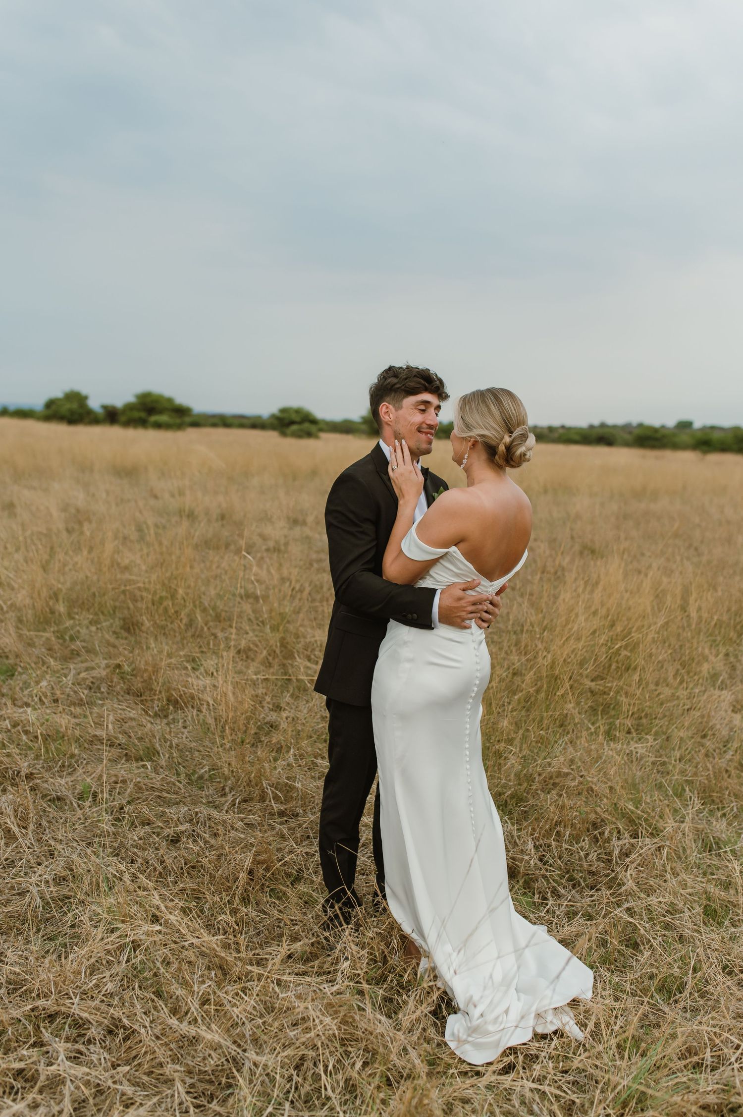 A romantic wedding photoshoot in a natural grassland setting with soft lighting.
