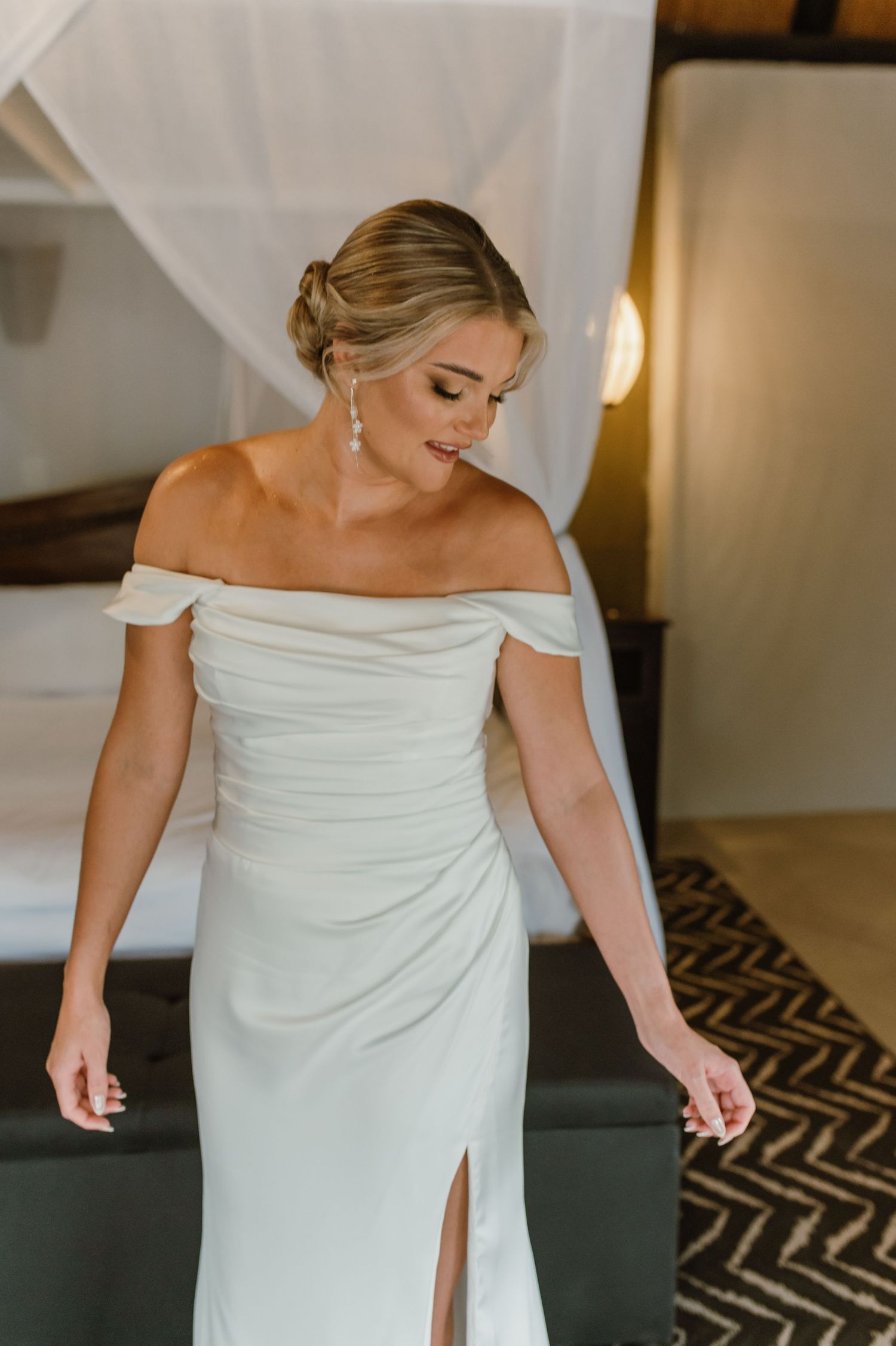 Candid moments of wedding dress preparation in a modern bedroom setting.