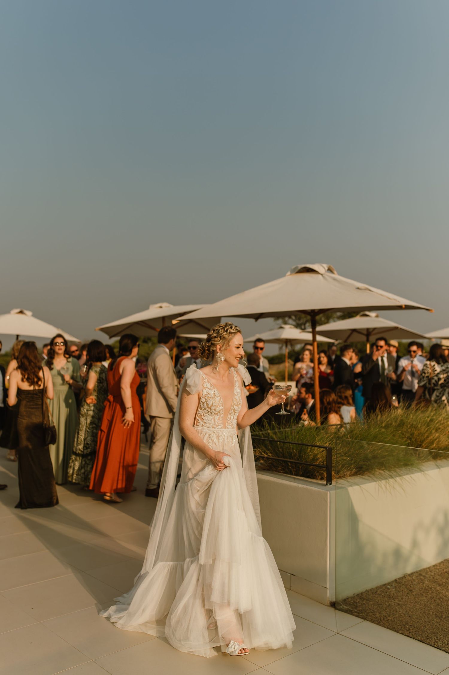 Outdoor wedding reception with guests gathered under white umbrellas at sunset.