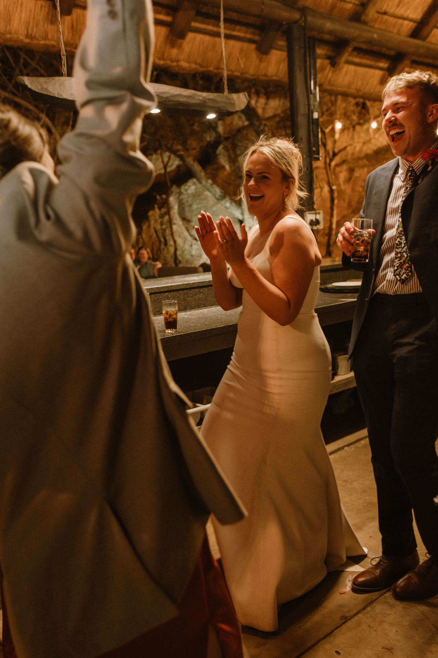 Wedding guests celebrate joyfully in a rustic barn venue with wooden beams and warm lighting.