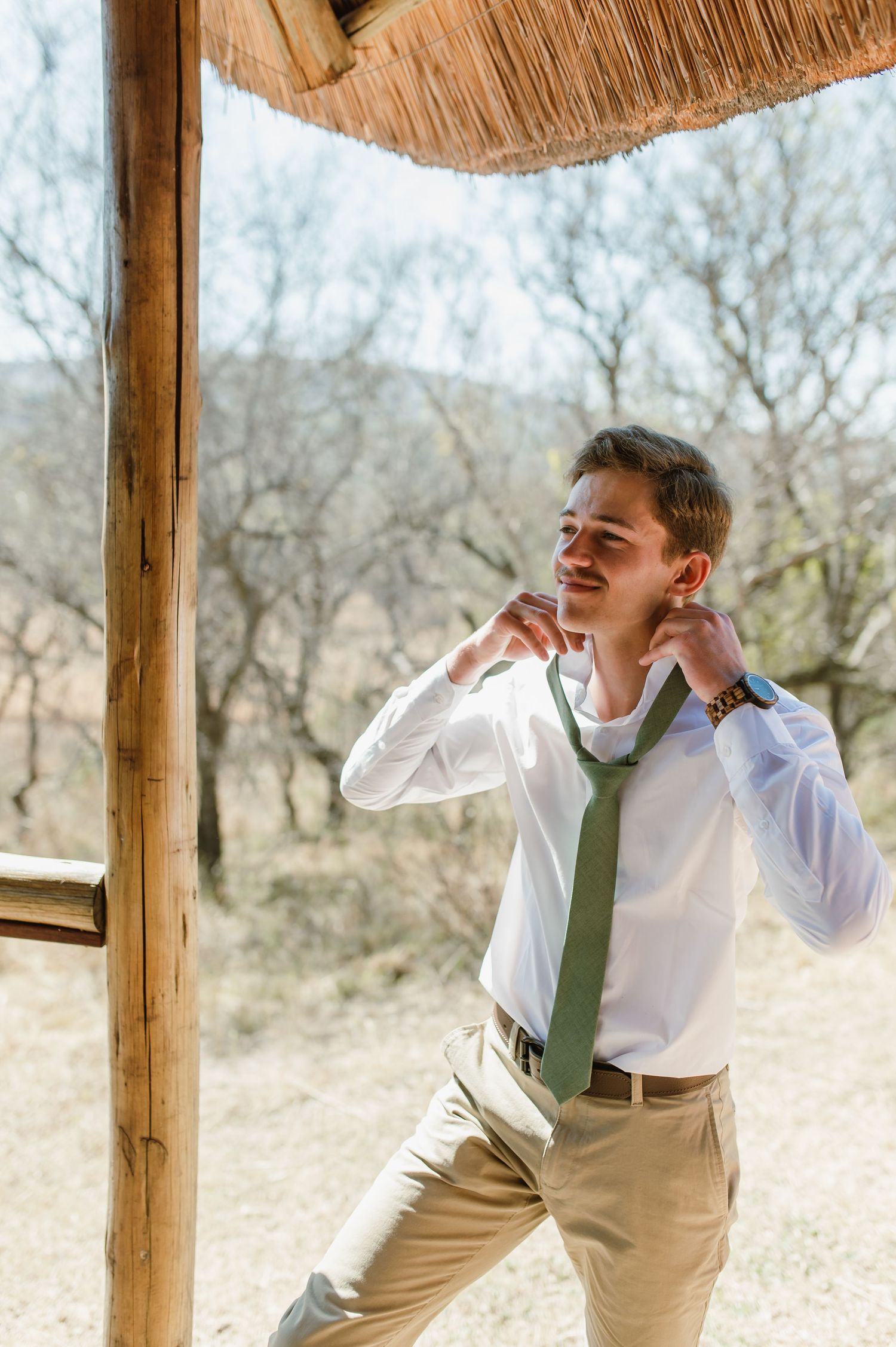 Person in white shirt and green tie getting dressed in outdoor gazebo.