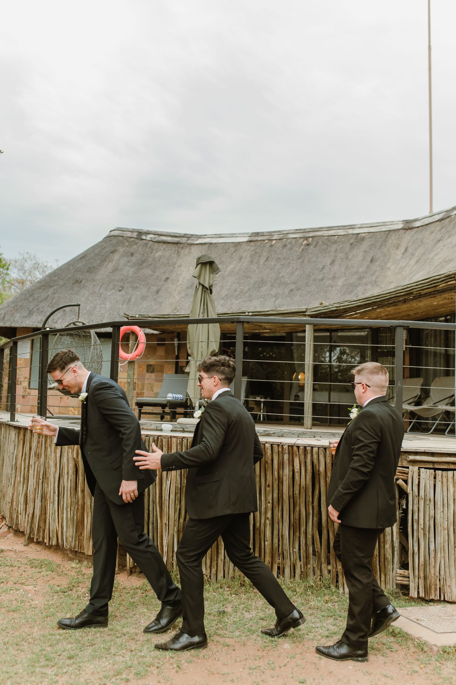 Wedding party members in formal attire walking in a playful line formation outside.