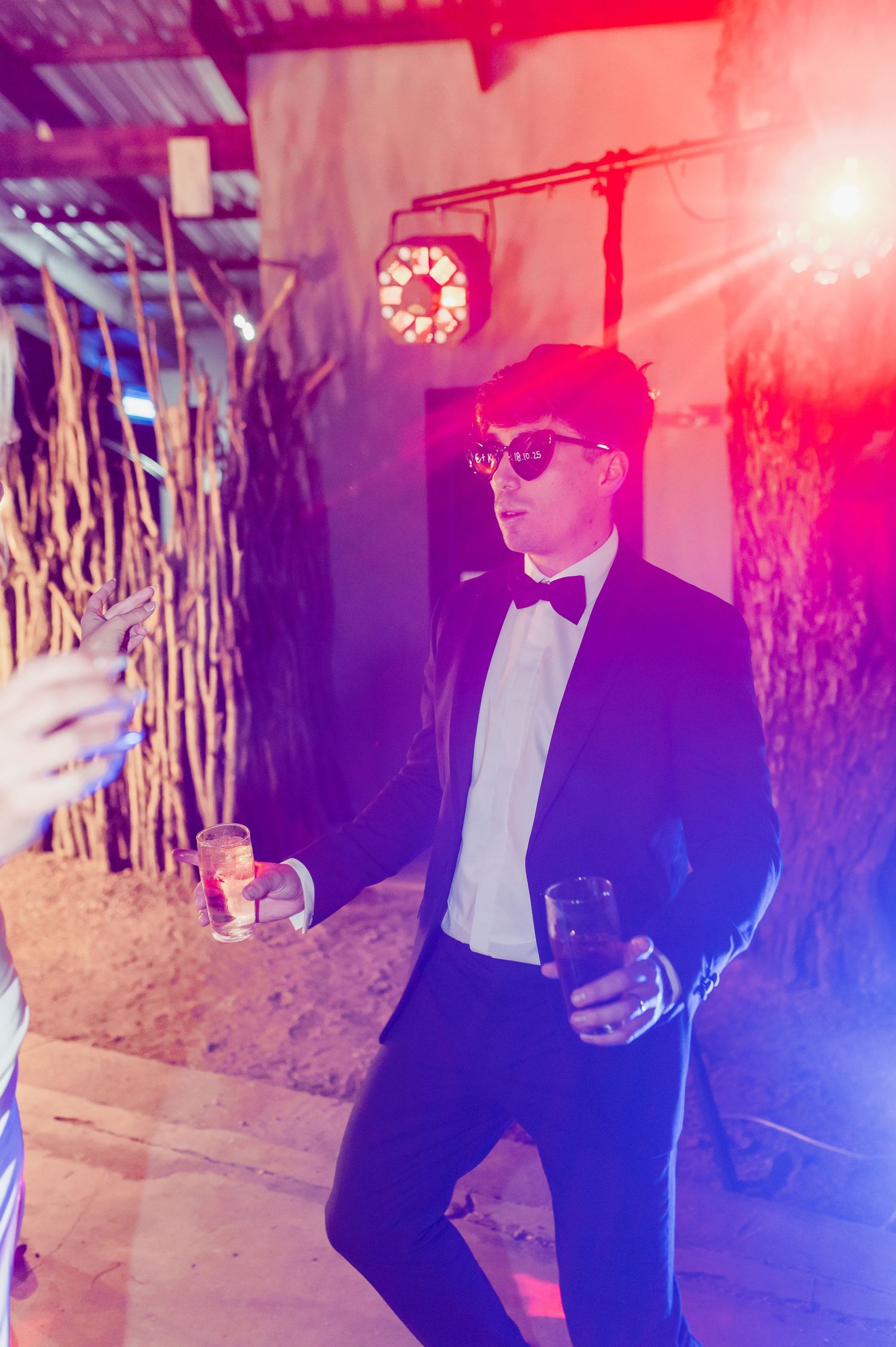 Person in formal attire dancing under dramatic purple and red lighting at a wedding reception.