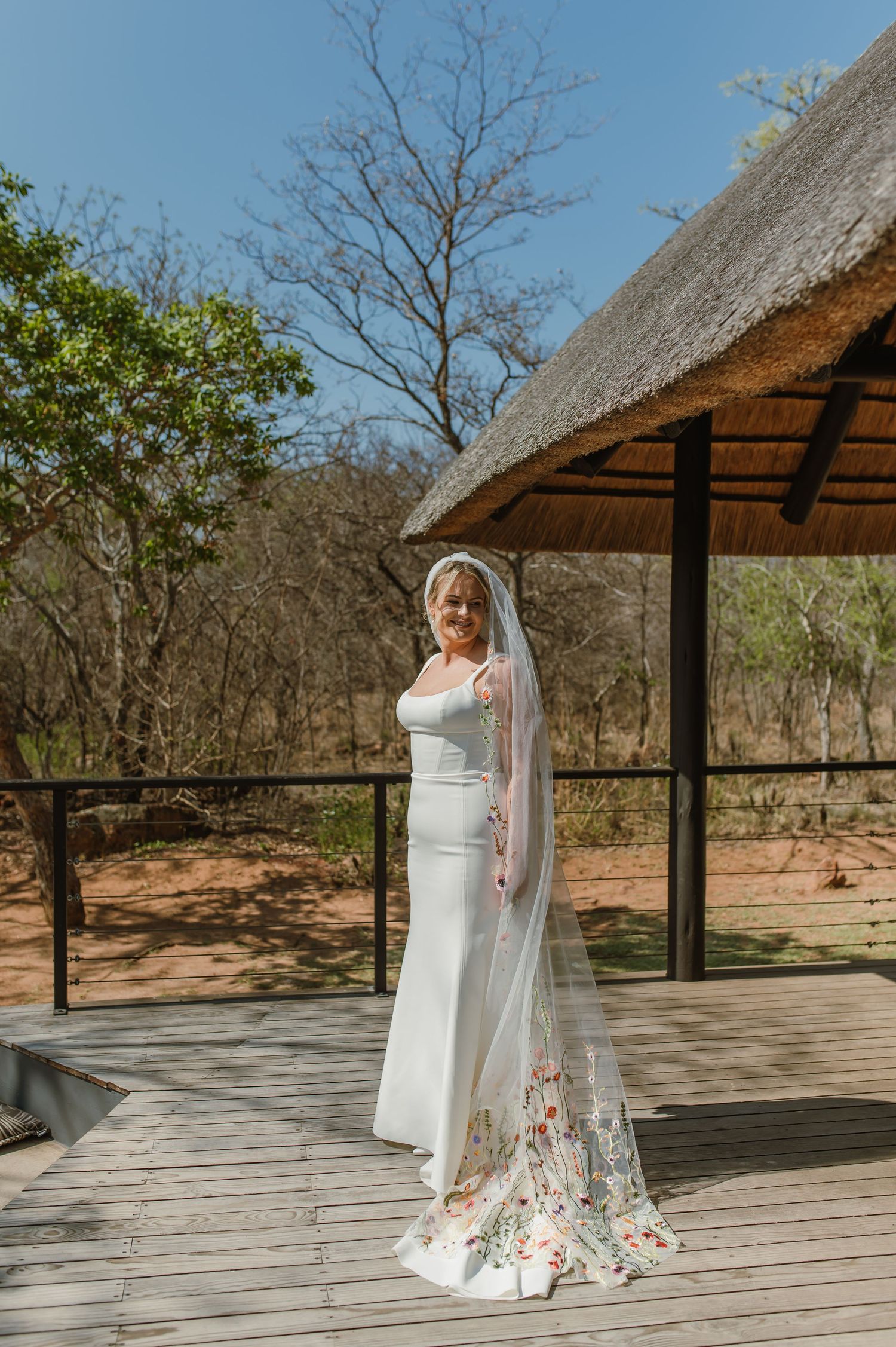 Outdoor bridal portraits on wooden deck with thatched roof gazebo in natural setting.