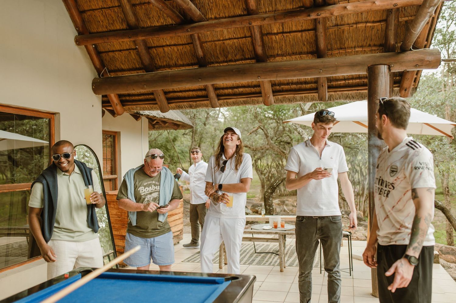 A group gathers outdoors on a rustic patio with wooden beams and natural surroundings.
