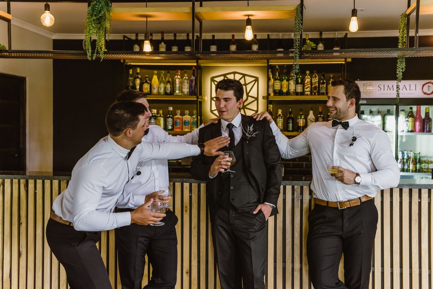 Wedding party members pose casually at modern indoor bar setting.