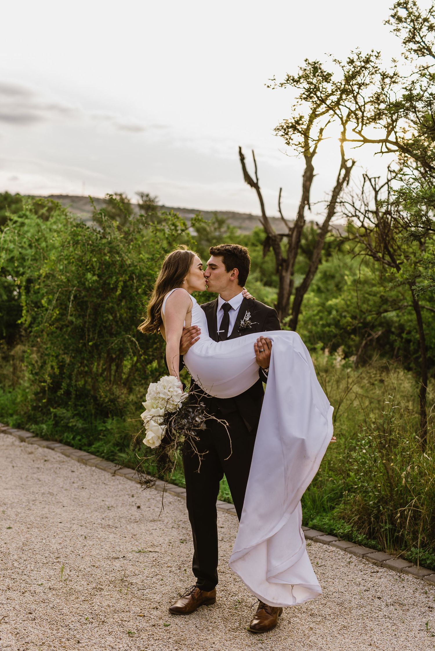Romantic couple shares intimate moments on a scenic outdoor path surrounded by greenery.
