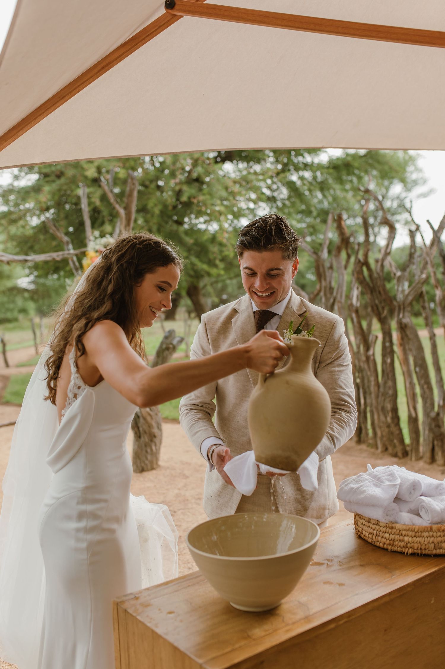 A couple makes pottery together at a wooden table in an outdoor setting.
