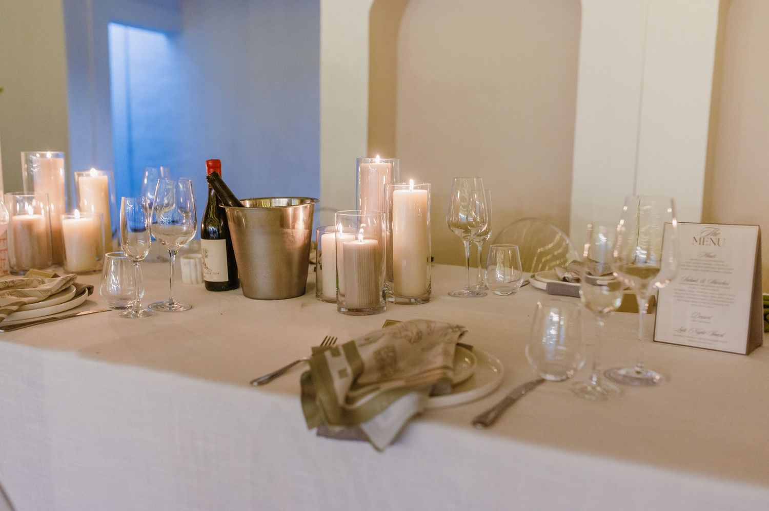 Elegant wedding reception table settings with white linens and glowing candle centerpieces.