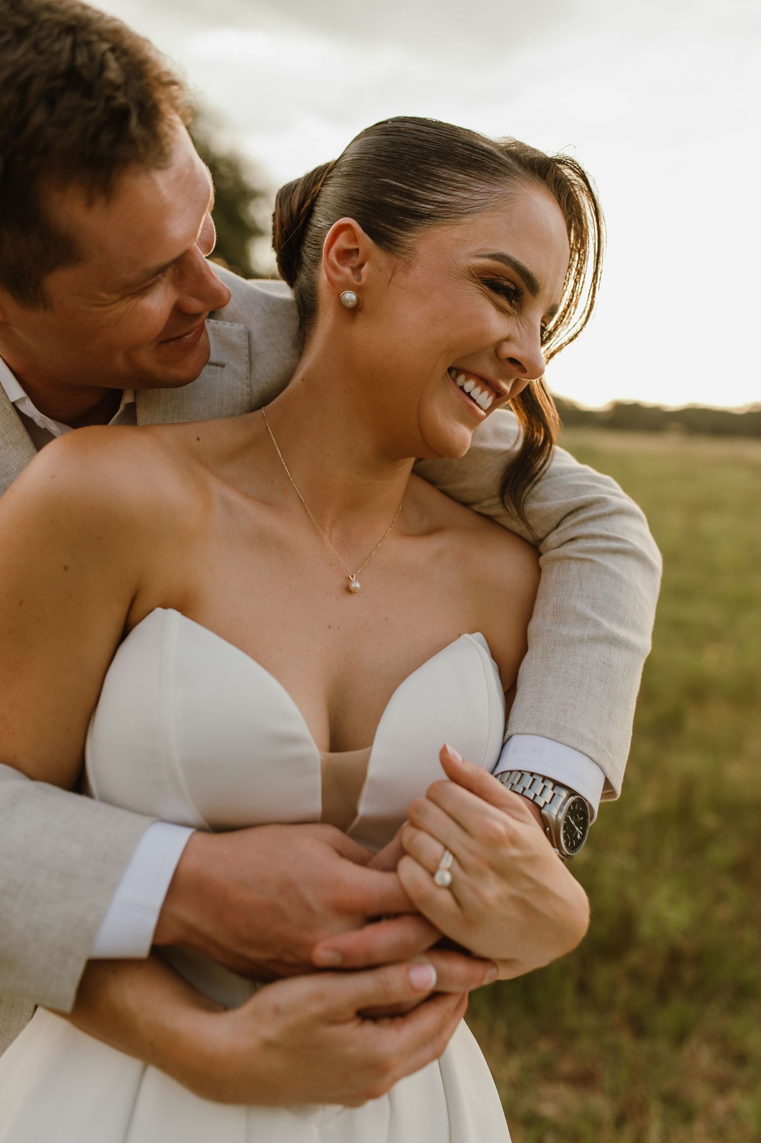 Intimate wedding portrait of a couple embracing and laughing in a golden field.