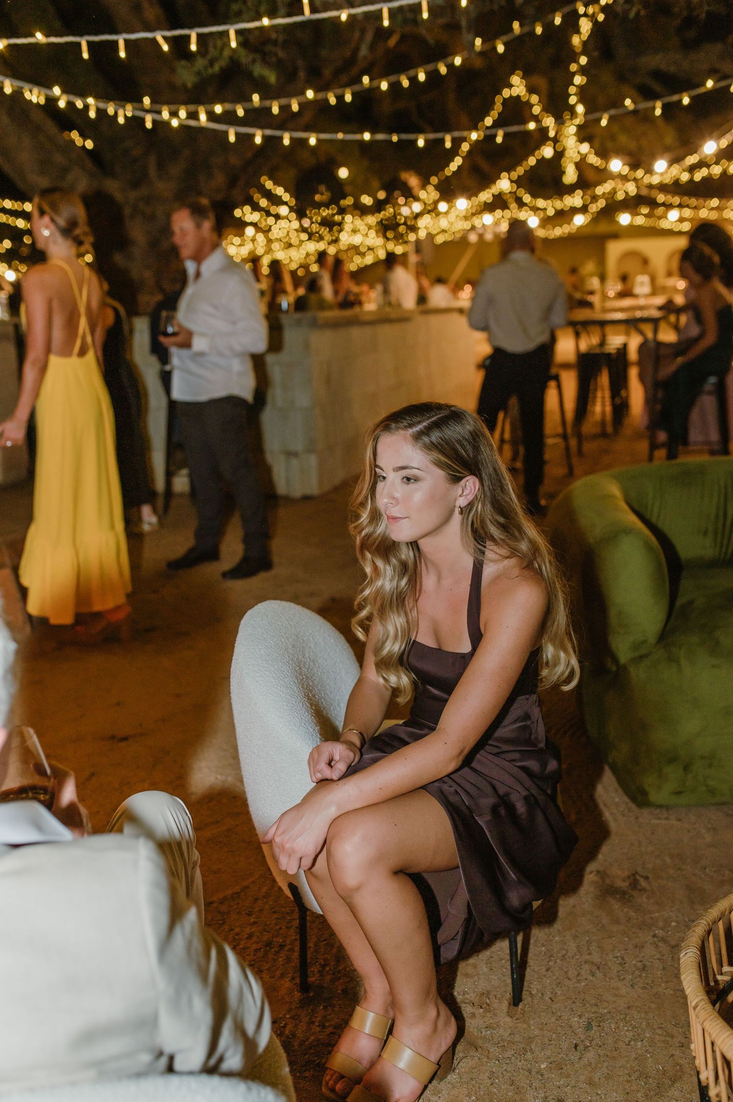 Evening wedding reception with string lights and guests mingling near vintage furniture.