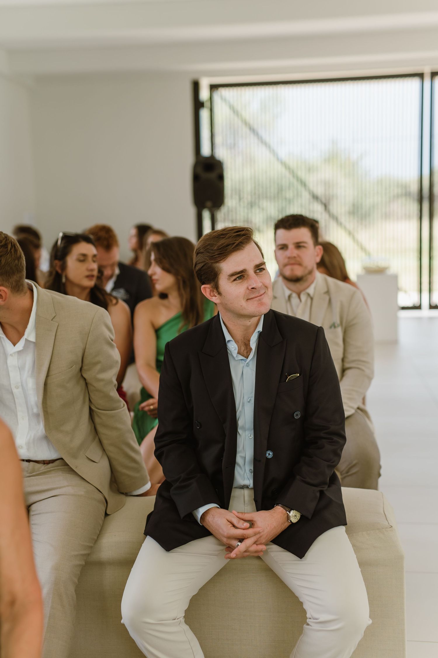 Wedding guests seated in rows at a modern minimalist venue with large windows.