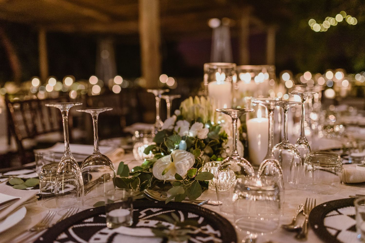 Elegant wedding reception table setting with white linens, floral centerpieces, and glowing candles in a rustic venue.