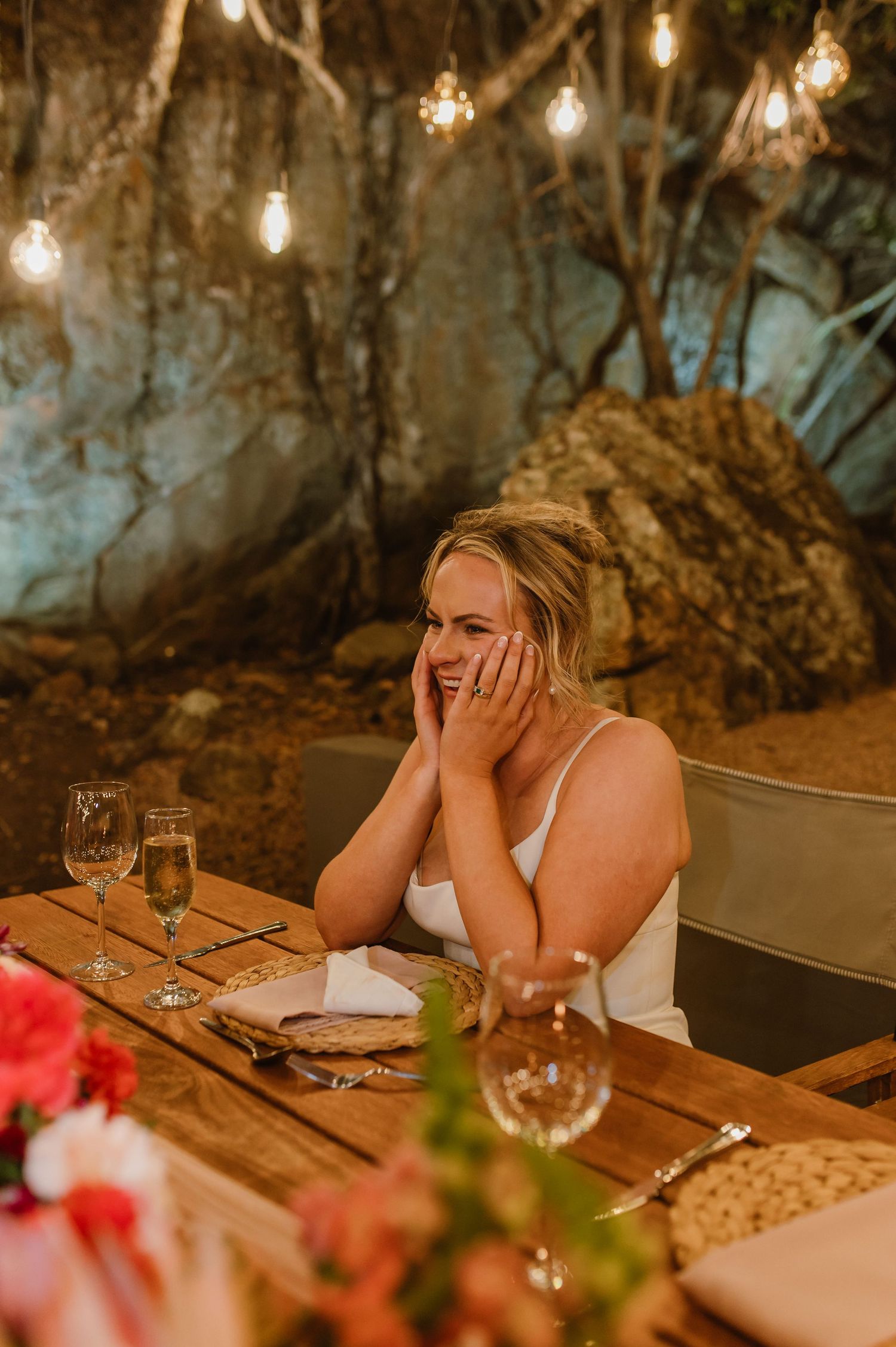 Intimate outdoor dining scene with warm lighting and floral arrangements on wooden tables.