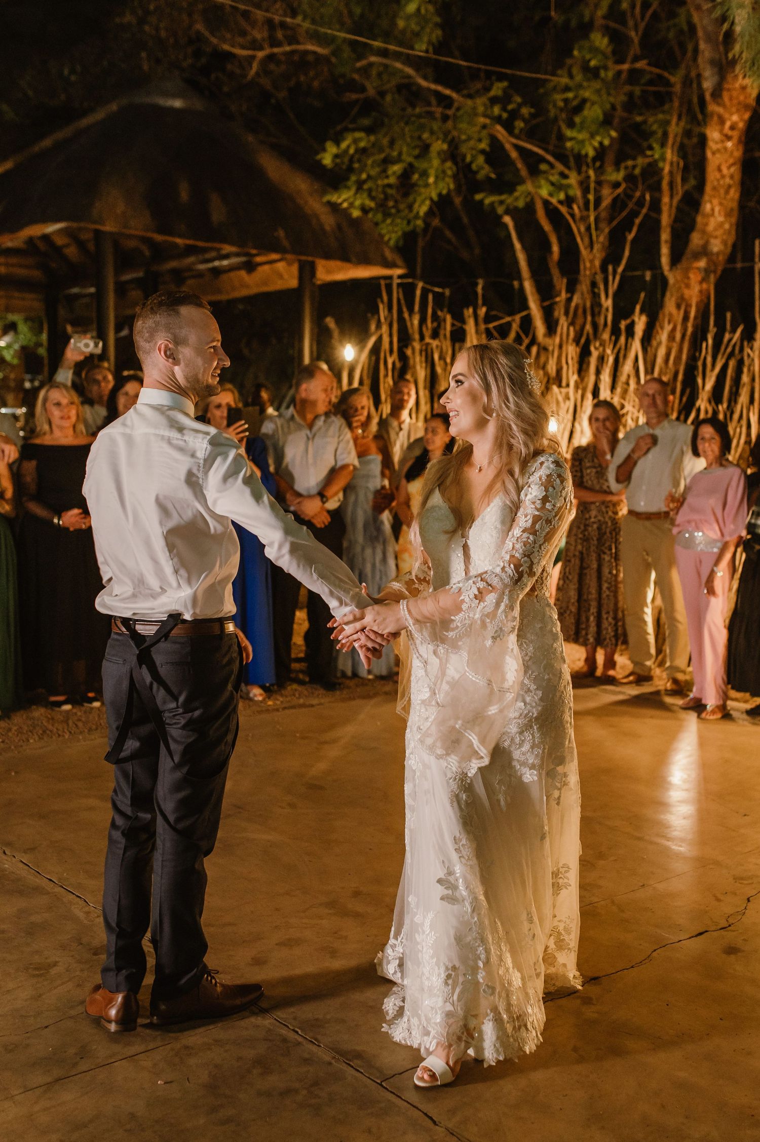 A couple dances together on an outdoor dance floor surrounded by guests and ambient lighting.