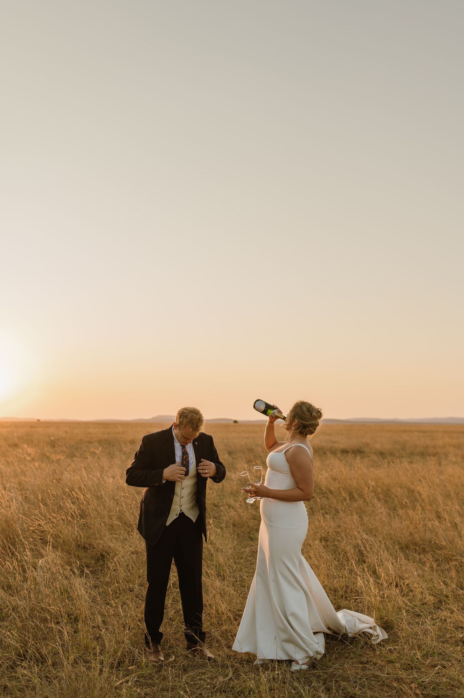Newlyweds celebrate with champagne in a golden wheat field at sunset.