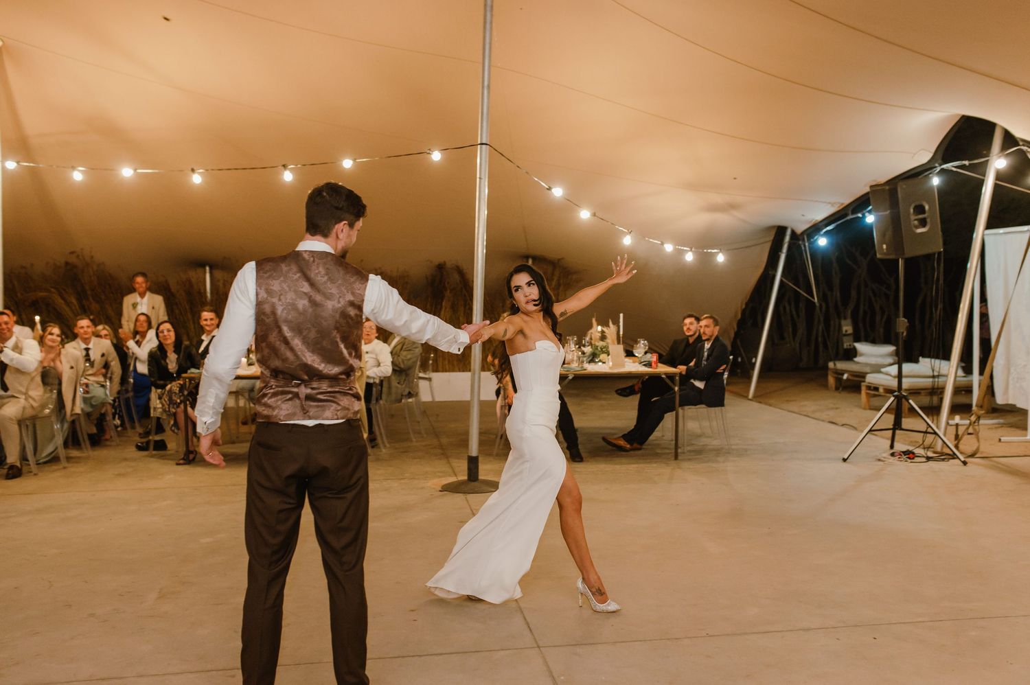 Couples dancing at wedding reception under warm tent lighting and string lights.