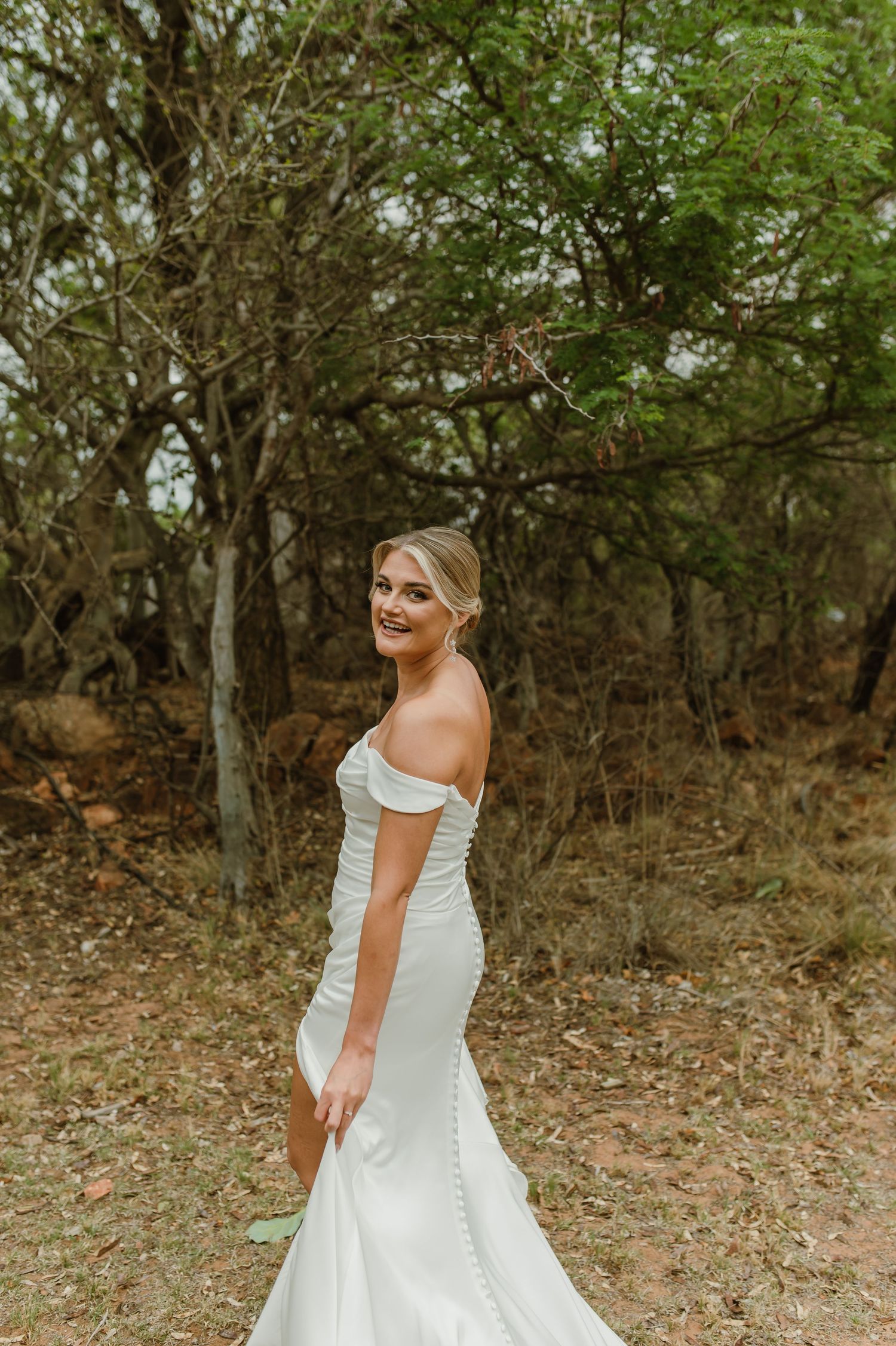 Classic mermaid wedding gown with off-shoulder detail photographed in rustic outdoor setting.